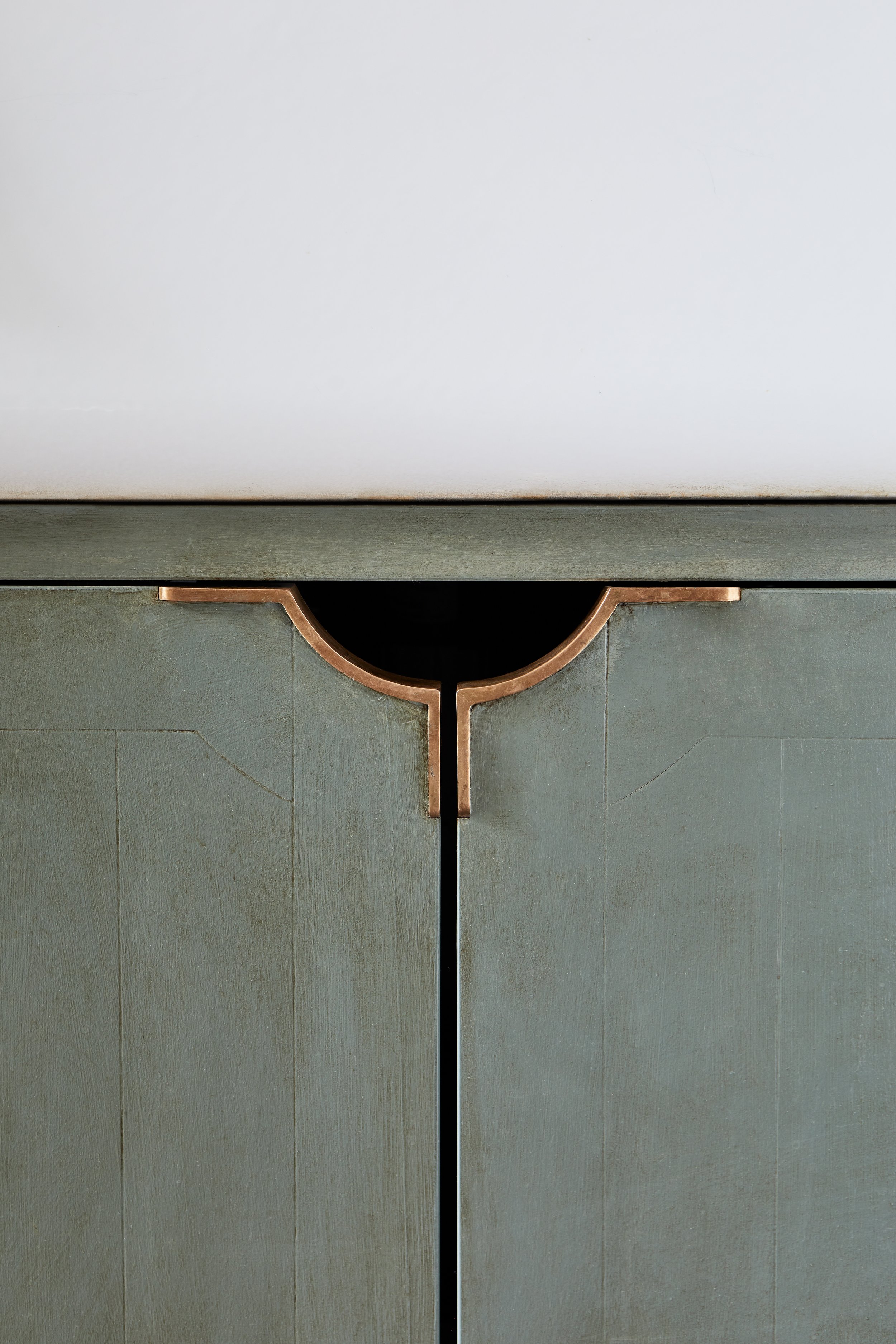 Photo of MORAY cupboard pulls on a cupboard under the sink, with the right and left handles forming a semi-circle matching the drawer pull, set against hand-painted aged green door panels.