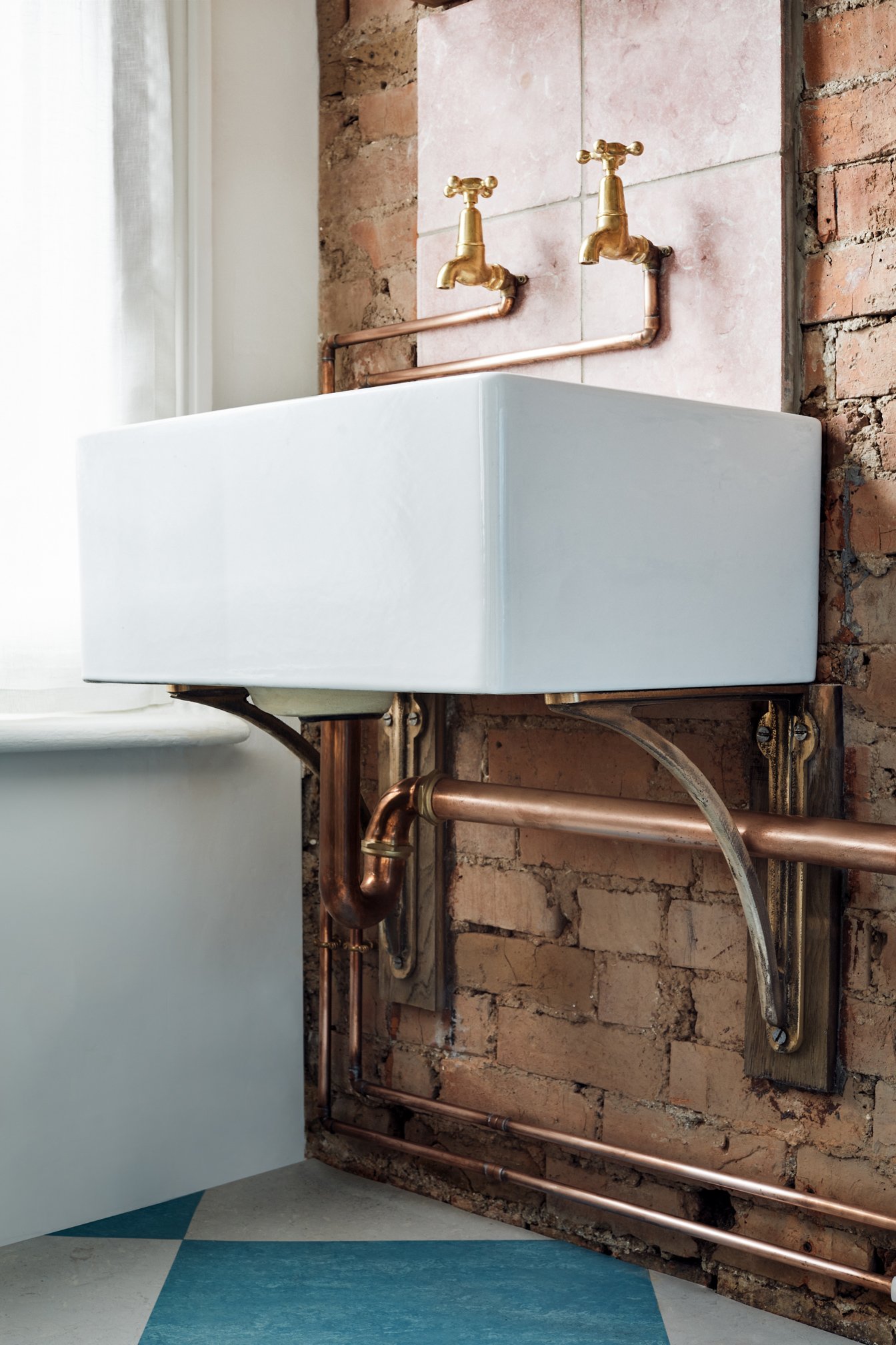Cast Bronze Sink Brackets – Small, Medium & Large | Small bracket supporting a Belfast sink in an industrial kitchen, fixed to a brick wall. Unlacquered bronze with a raw, aged patina.