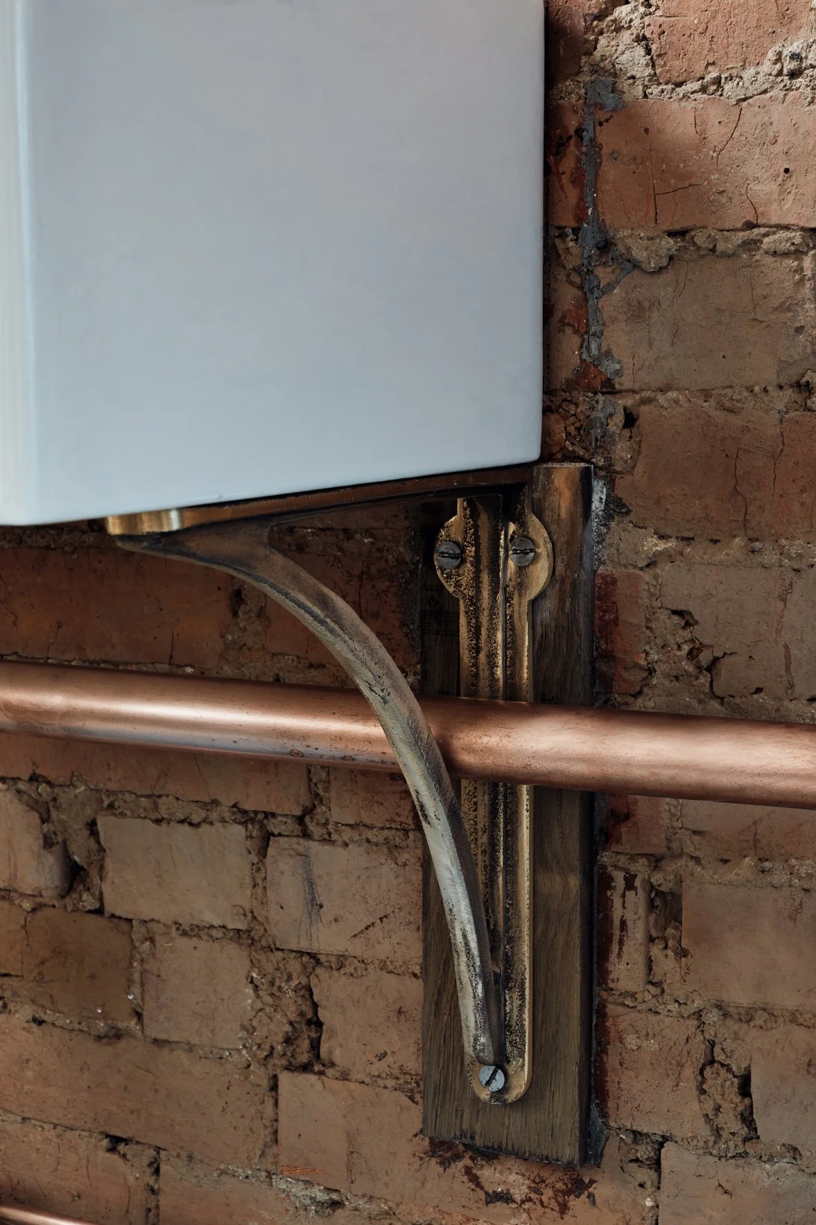 Cast Bronze Sink Brackets – Small, Medium & Large supporting a Belfast sink in an industrial kitchen, close-up side view. The small bracket is fixed to a brick wall, showcasing its sturdy design.
