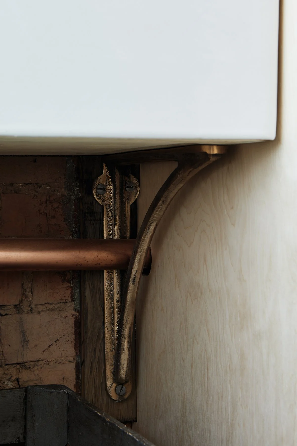 Cast Bronze Sink Brackets – Small, Medium & Large supporting a Belfast sink in an industrial kitchen, close-up side view. The small bracket is fixed to a brick wall next to a plywood unit.