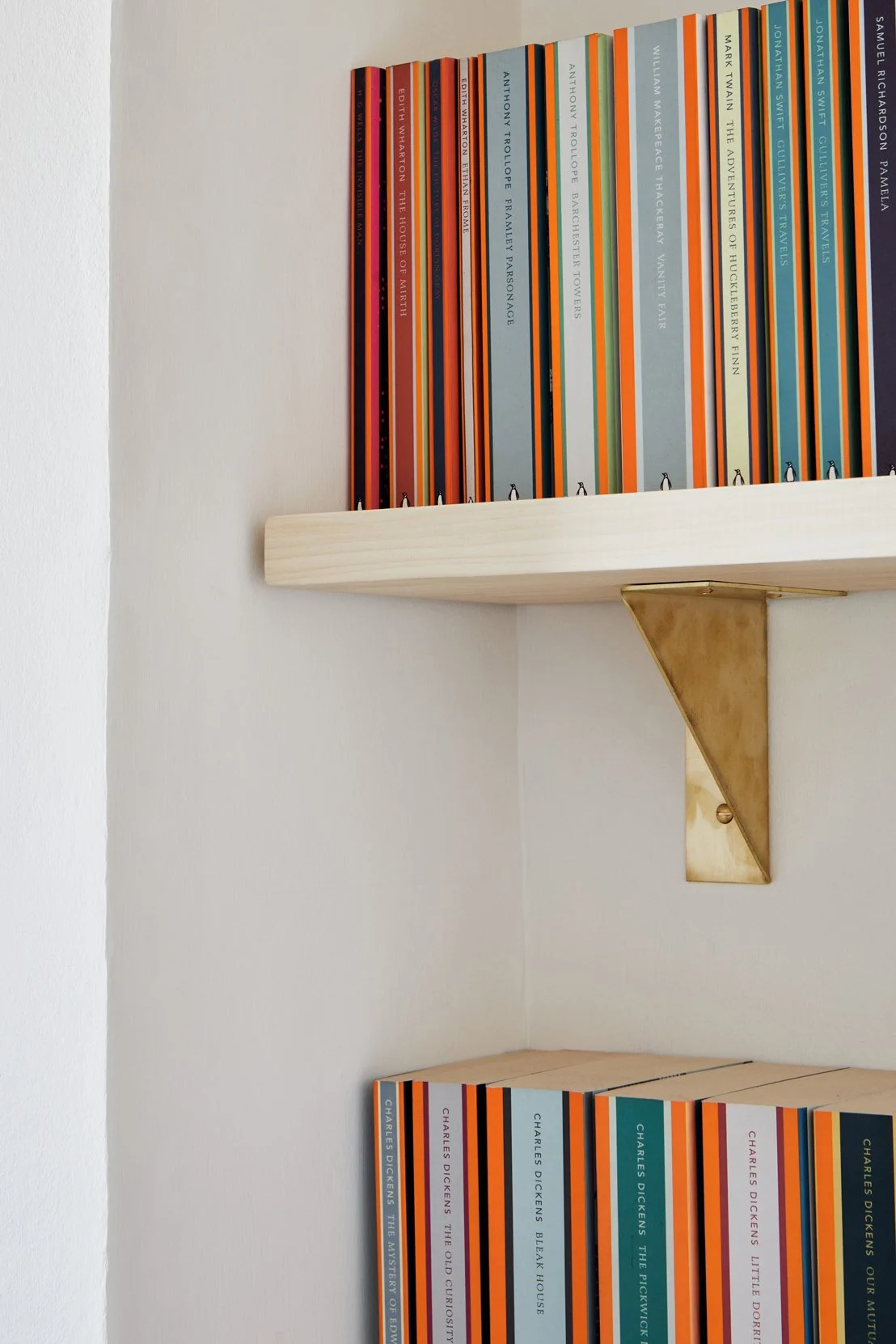 Close-up of the right-hand brass folded bracket supporting a timber shelf filled with Penguin Classics books. The unlacquered brass ages beautifully over time.