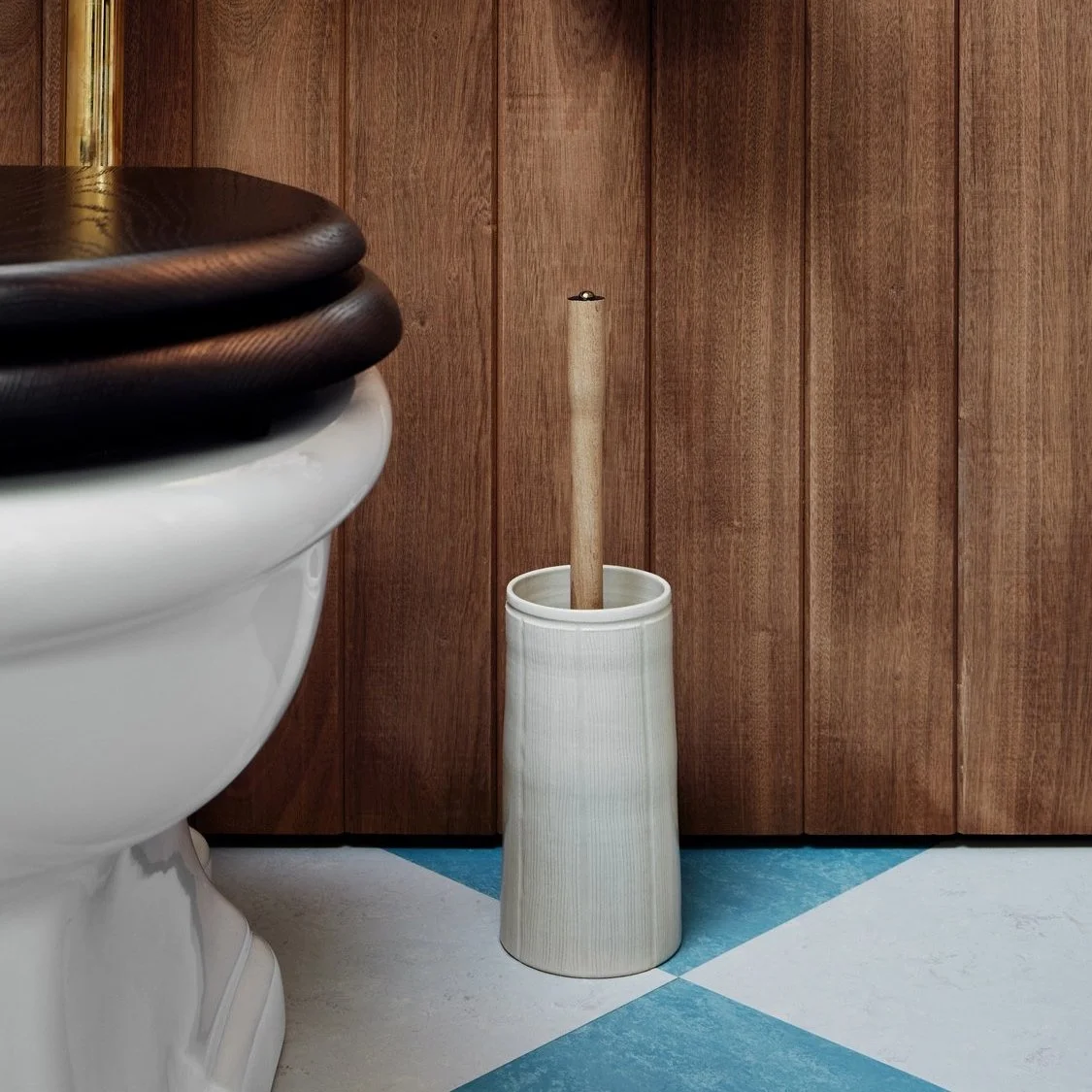 Toilet Brush Holder in stoneware sits next to a toilet on a blue and white diamond bond tiled floor, with sapele hardwood cladding covering the wall in the background.