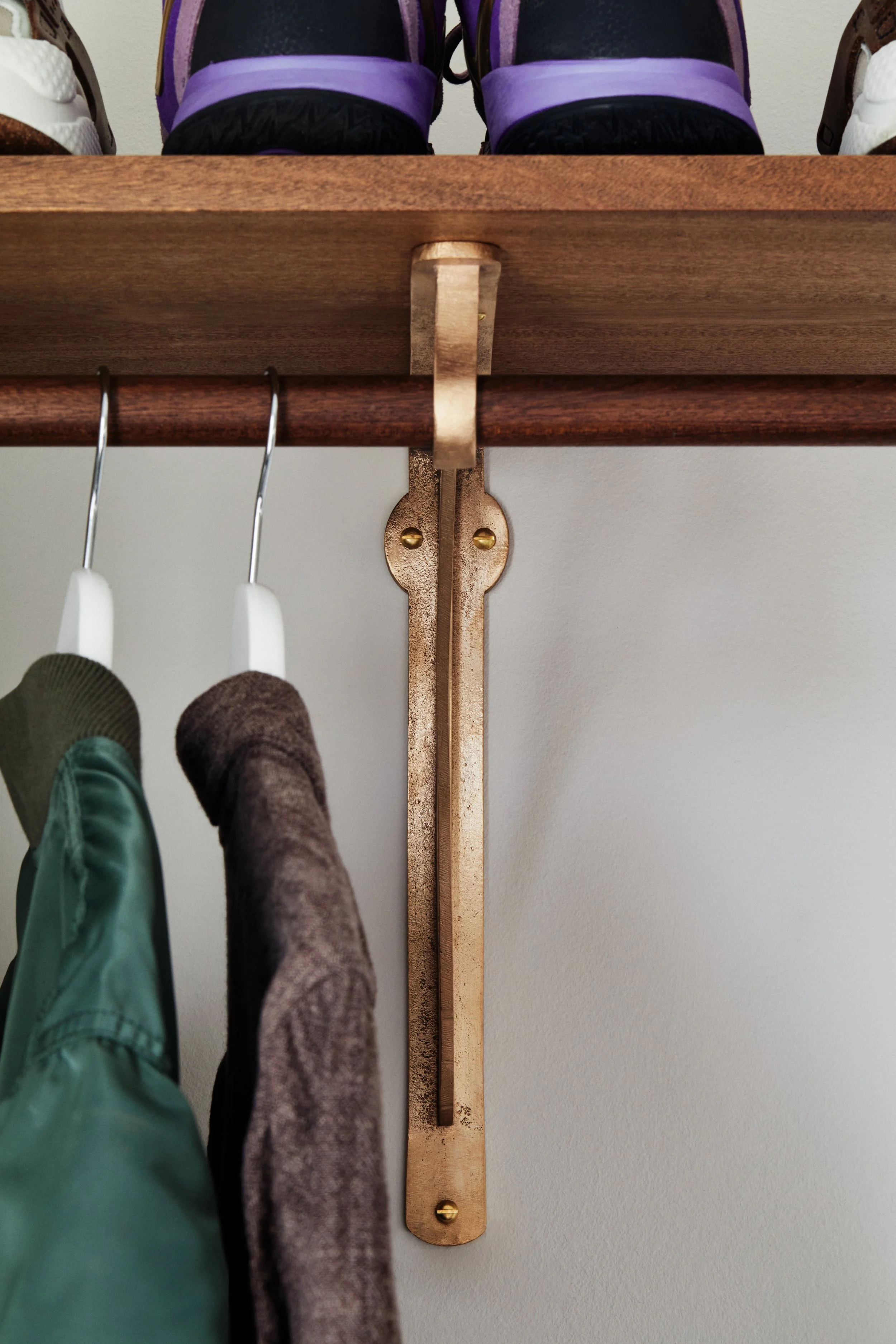 wardrobe bracket shot straight on made in raw bronze. two hanging jackets are visible side on.