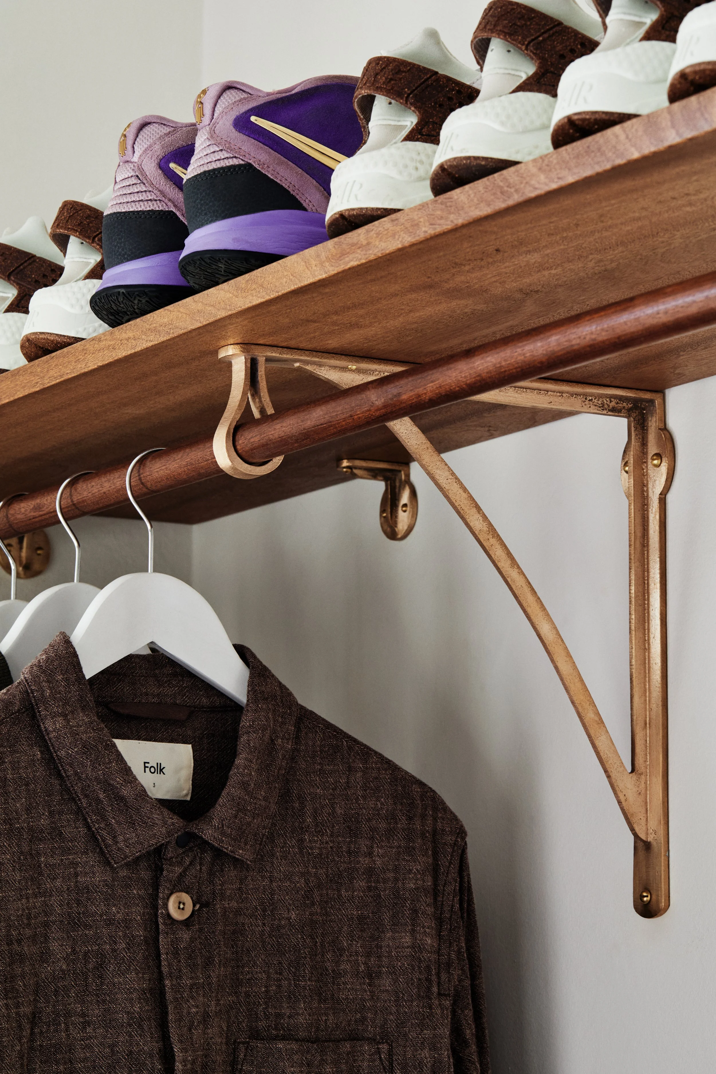 wardrobe bracket bracket supporting timber rail below and timber shelf above made in raw bronze. nike shoes sit on the shelf and a linen jacket hangs from the rail