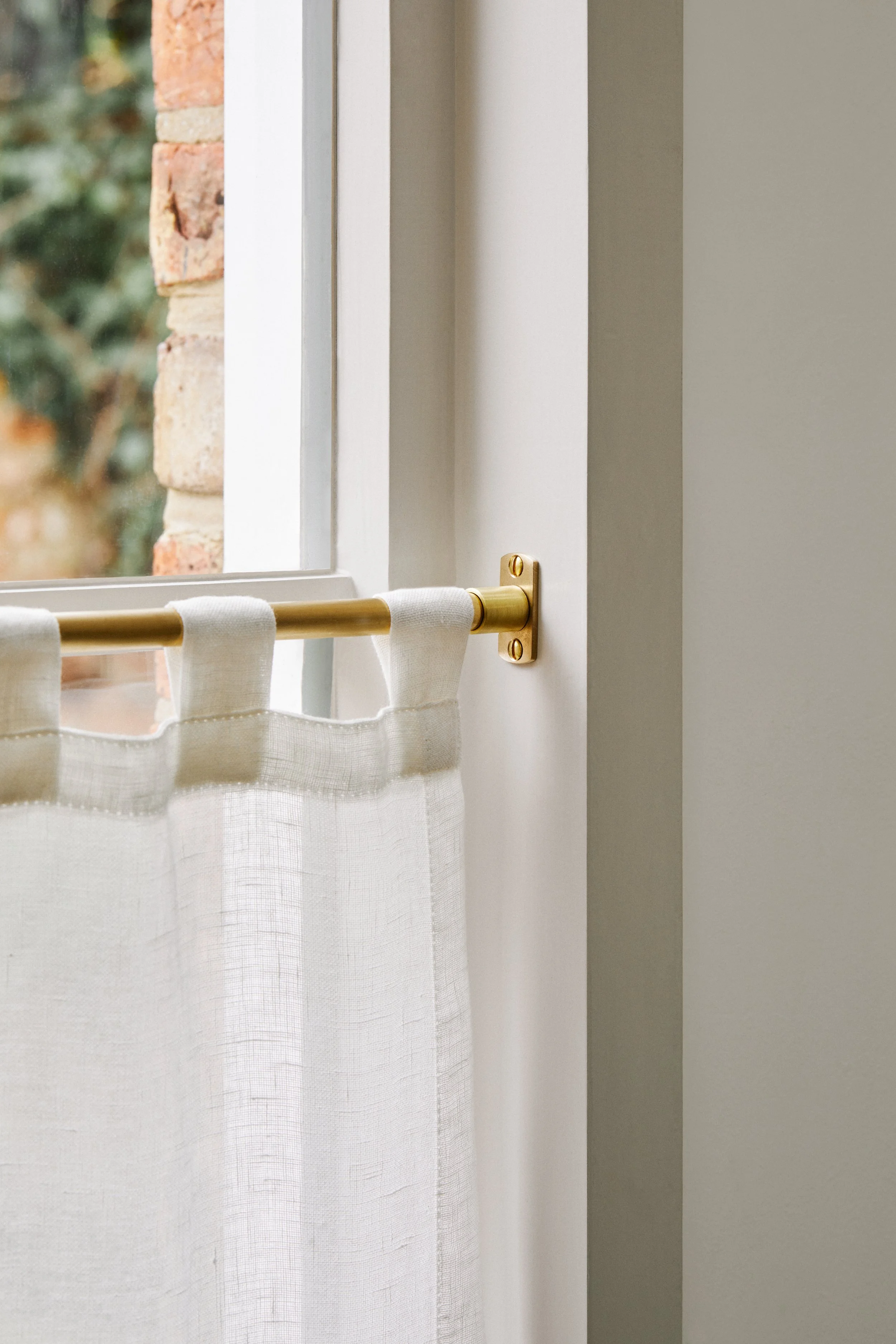 Unlacquered Brass Café Curtain Rail Set with Recessed Brackets mid shot of end bracket fitted to kitchen window frame with 3 fabric loops hanging from brass rail to the left.