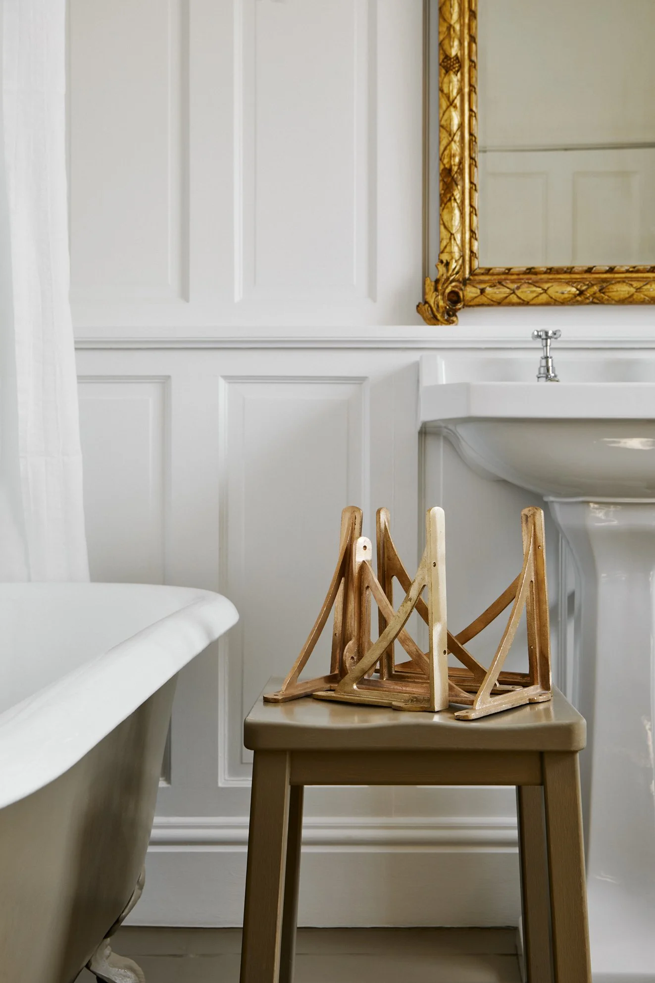8" Strong Boy Brackets in cast bronze artistically arranged on a painted wooden stool in a paneled bathroom. The edge of a rolltop bath is visible on the left, with a basin in the background.