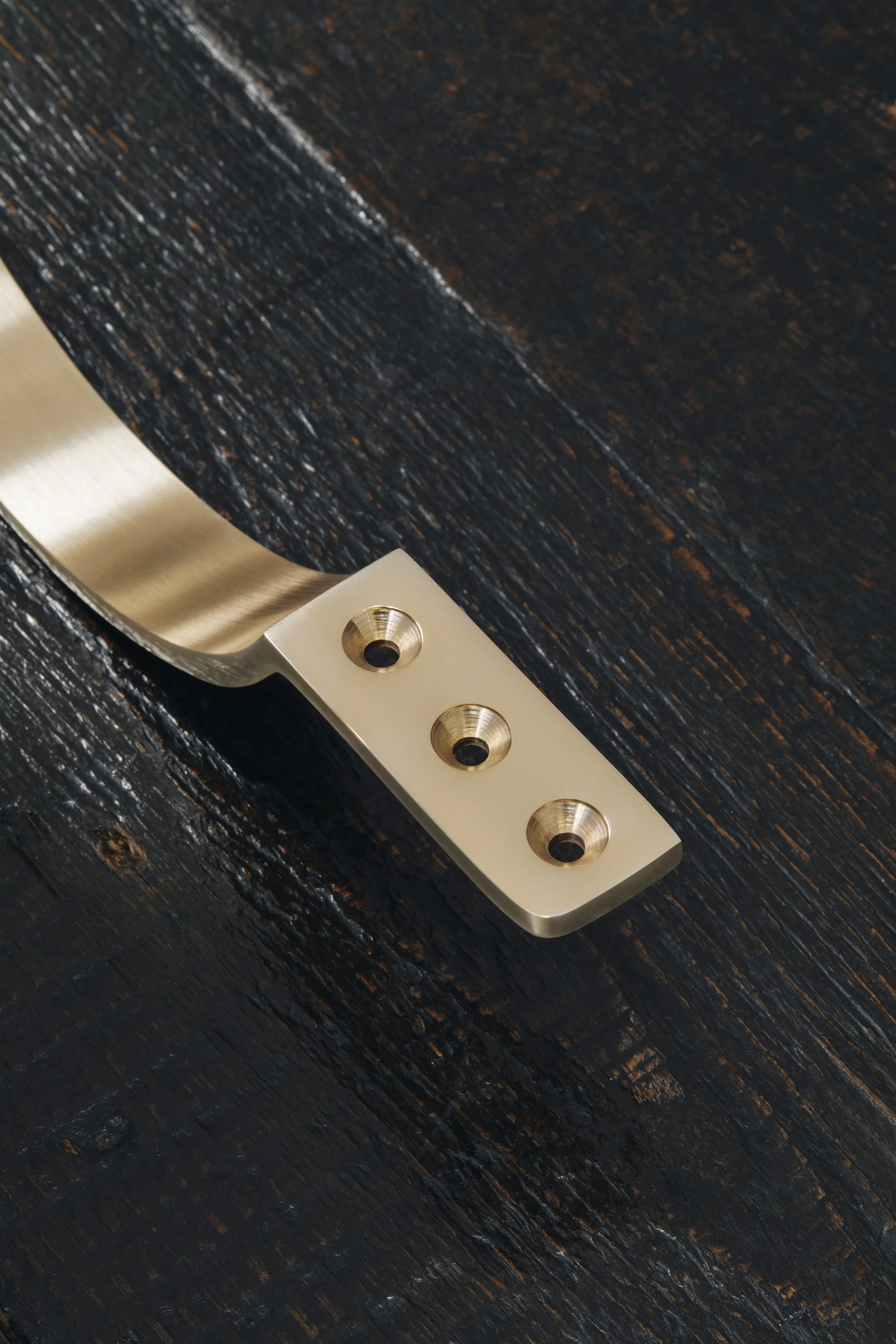 Close-up of 3 countersunk screw holes for a Moray drawer pull, showing only half the handle, resting on a dark timber display board, not yet fitted.