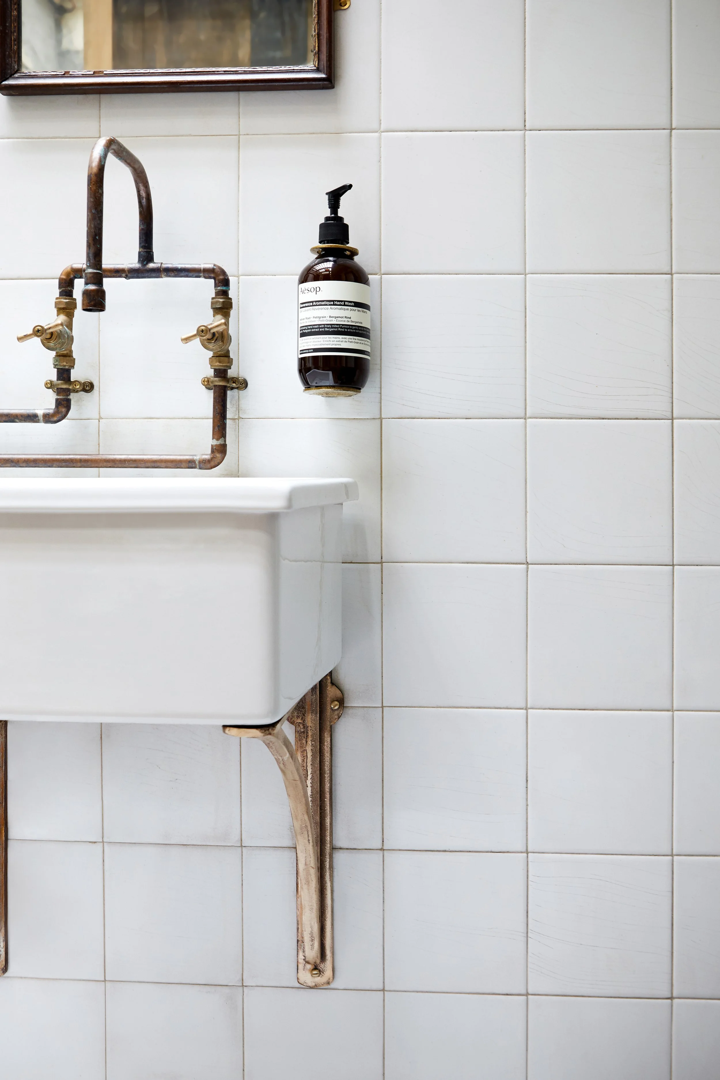 Cast Bronze Sink Brackets – Small, Medium & Large | Small bracket supporting a ceramic lab sink in a white tiled WC, fixed to a tiled wall. Unlacquered bronze with a raw, aged patina.