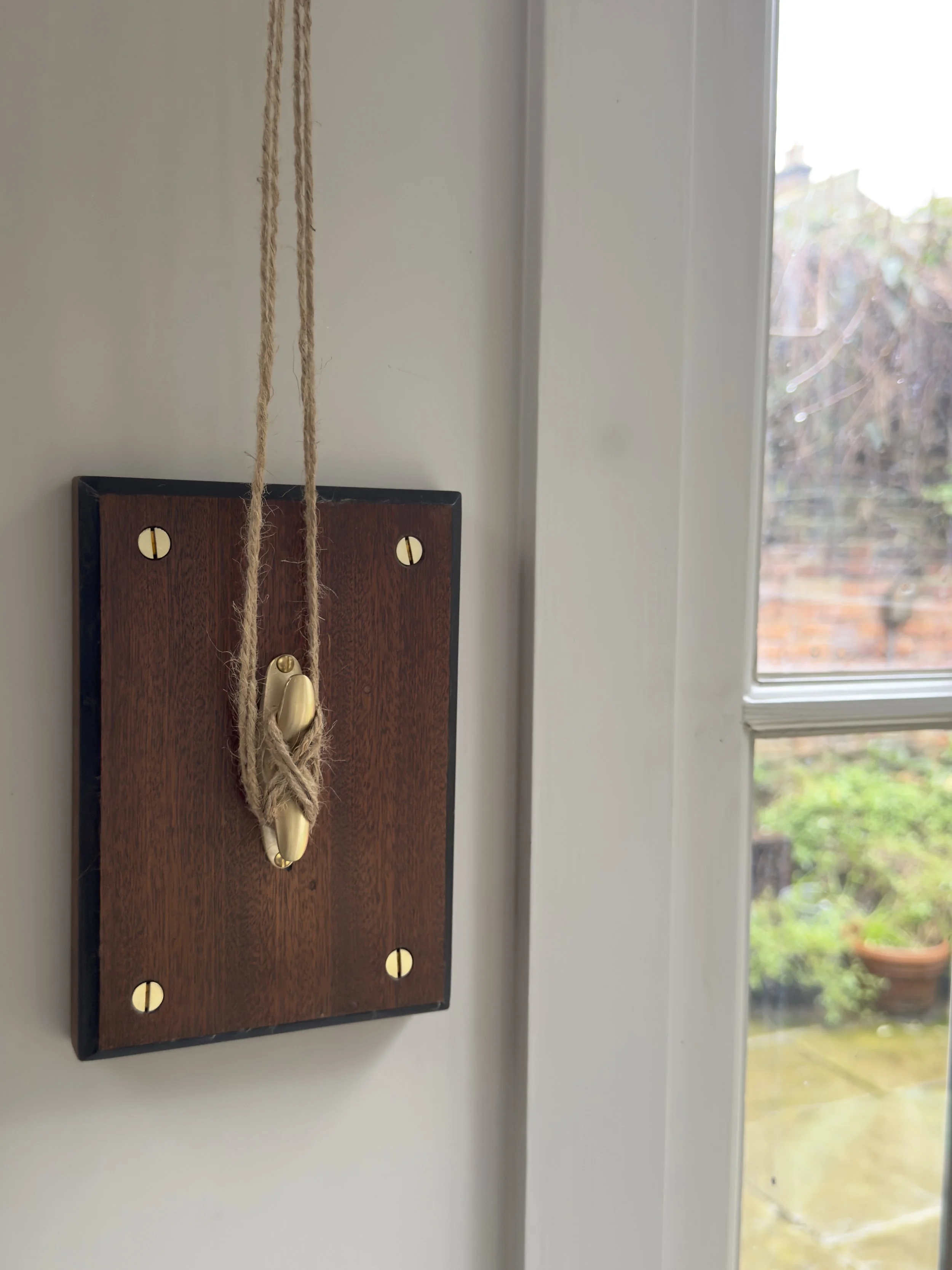 the-lewis-cleat-hook-unlacquered-brass-brown-timber-mounting-board-window-close-up.jpeg