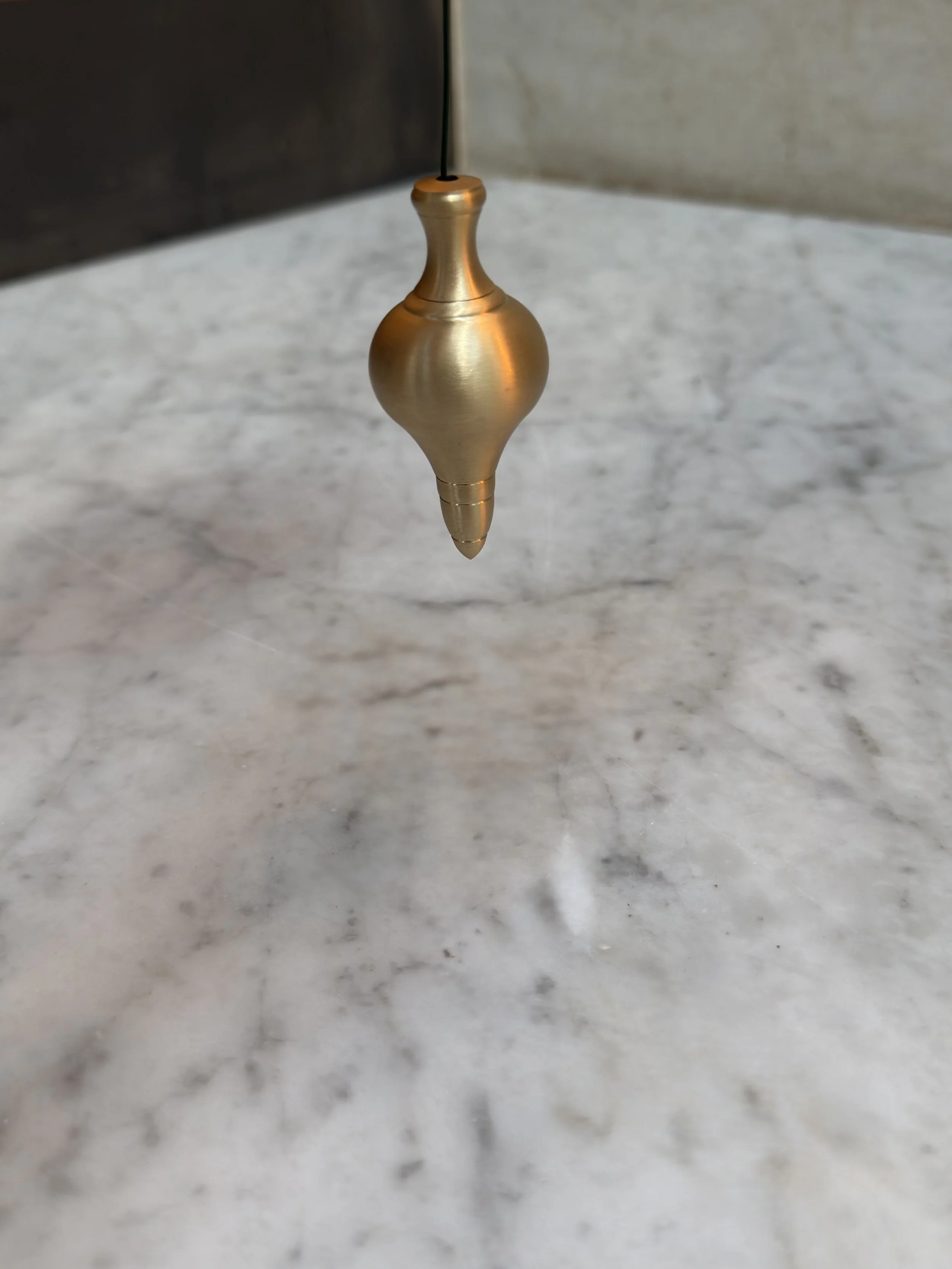 unlacquered-brass-cord-weight-suspended-above-marble.jpg