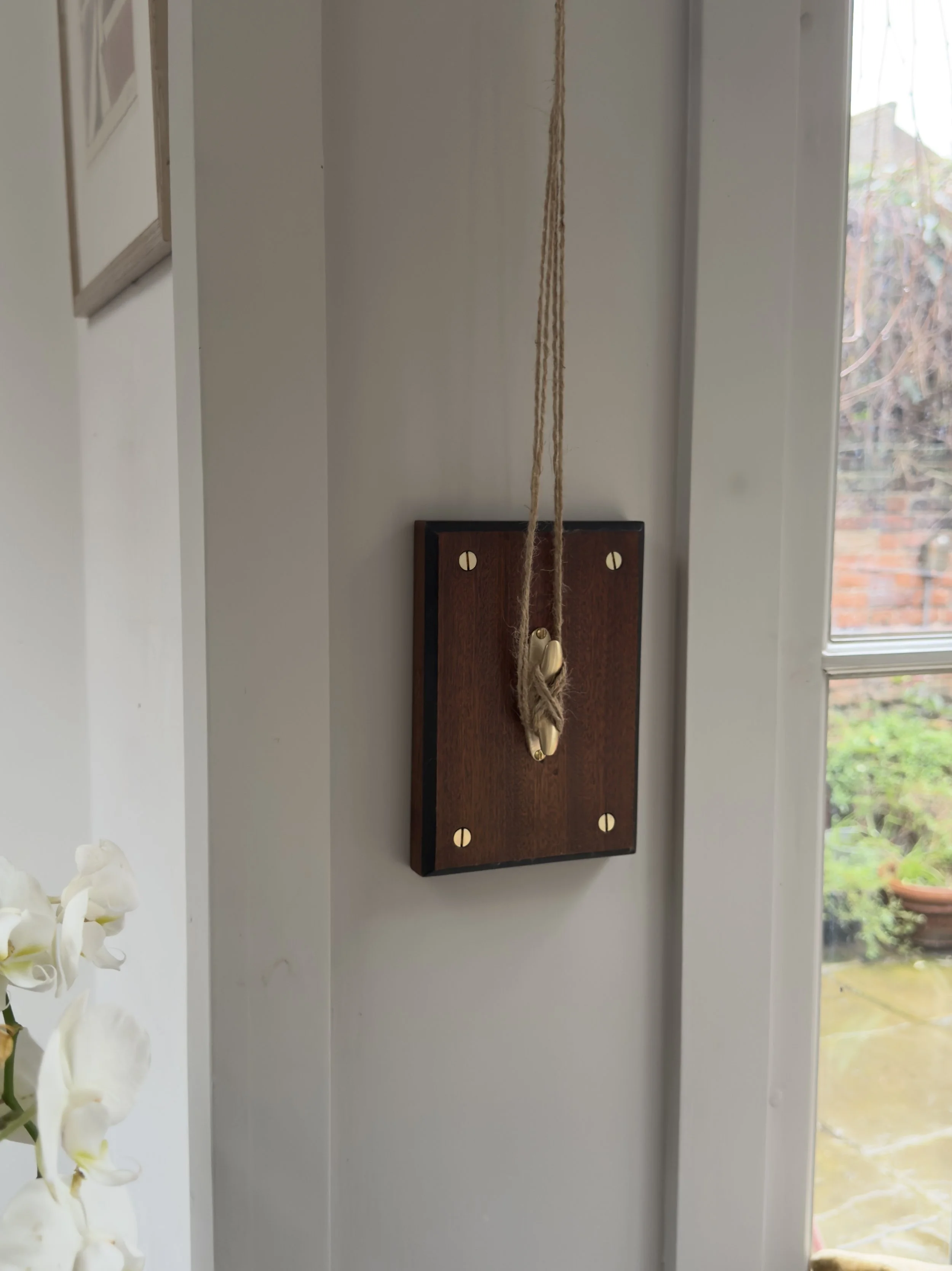 the-lewis-cleat-hook-unlacquered-brass-brown-timber-mounting-board-window-angled.jpg