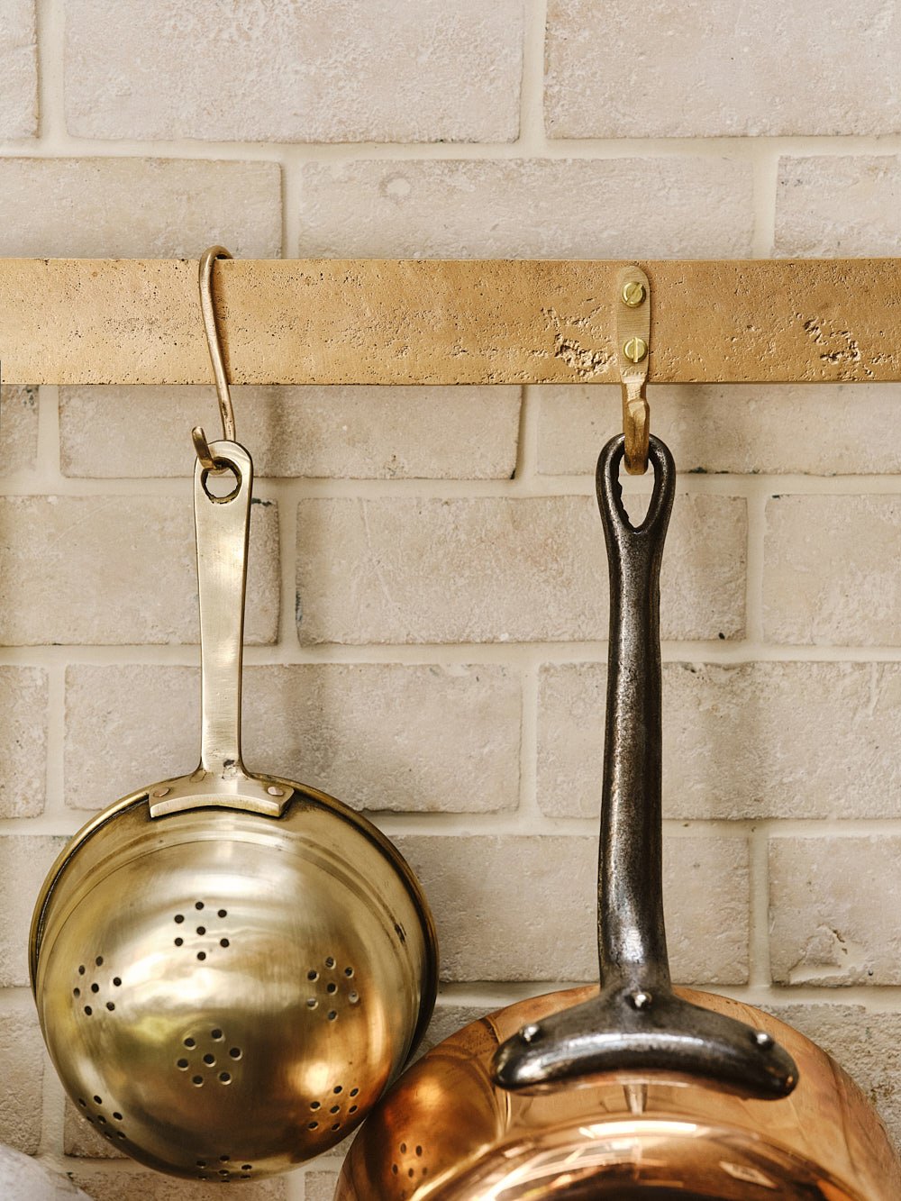 Close-up of the centre of the sand-cast bronze pan rack with pans hanging, showing the raw bronze finish and hook spacing.
