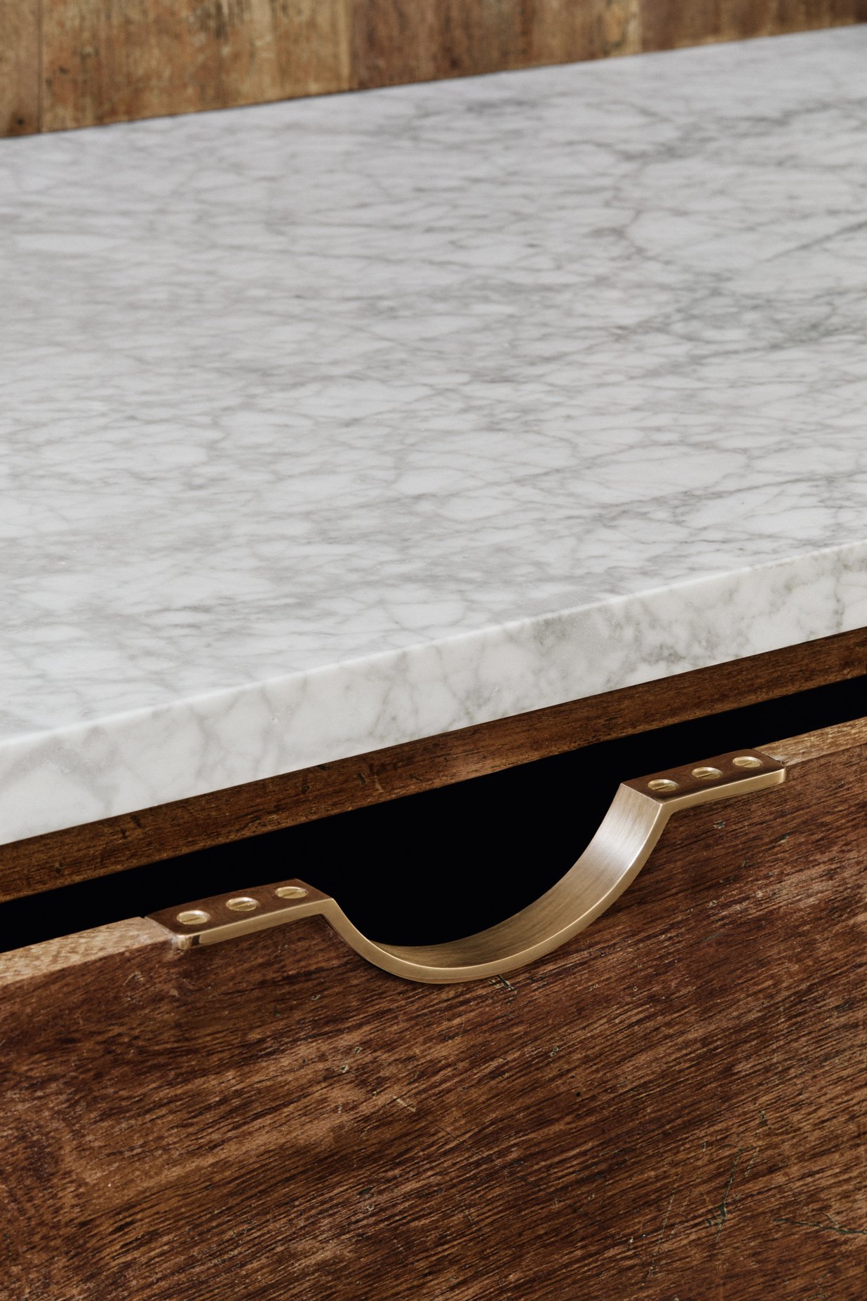 Close-up of the face of an ajar drawer with a Moray drawer pull in a reclaimed iroko kitchen, with a grey marble kitchen work surface visible at the top.