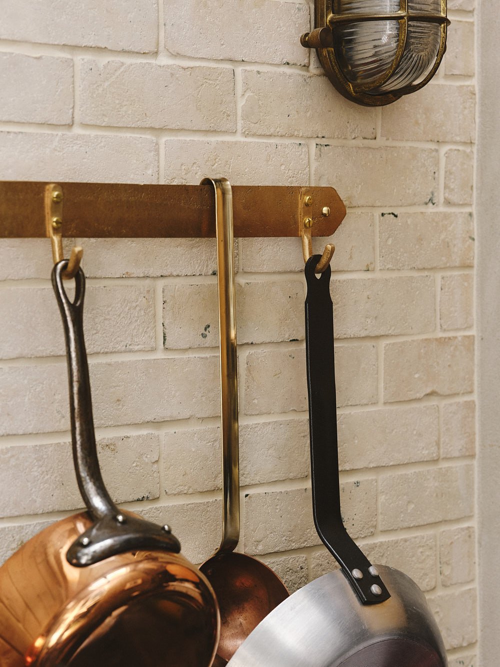 Angled close-up of the pan rack’s end hook with a hanging pan, highlighting the bronze patina and craftsmanship.