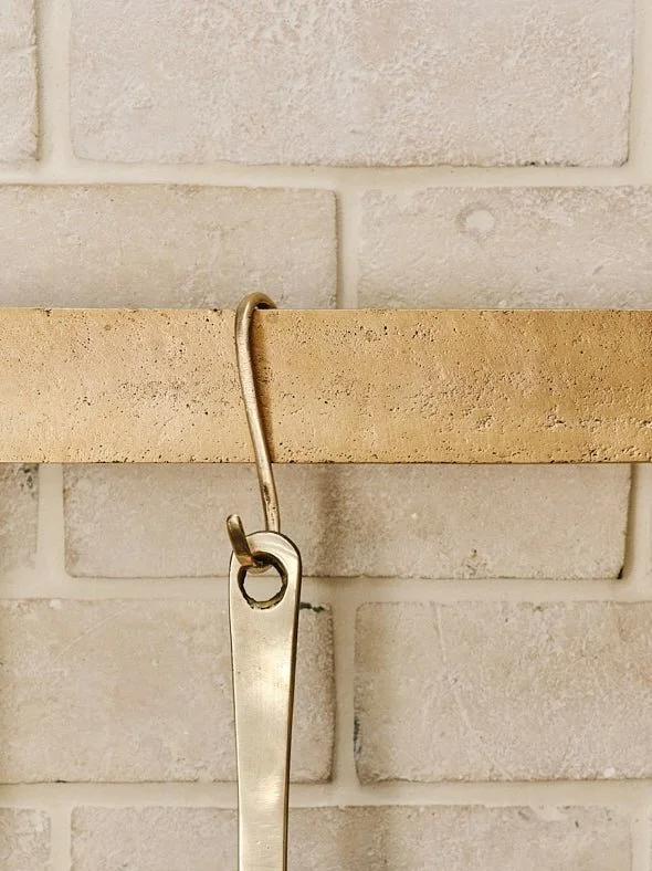 Close-up of a sand-cast bronze S hook at the centre of the pan rack, with a pan hanging to show the hook’s raw bronze detail and strength.
