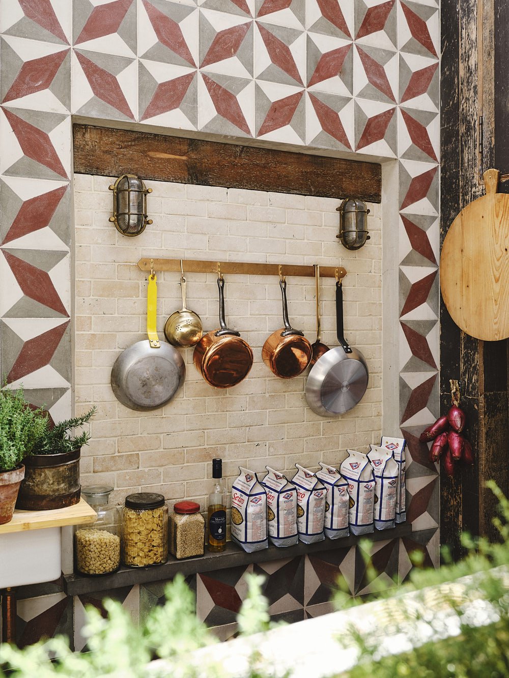 Wide angled larder shot of the sand-cast bronze pan rack with pans hanging, unlacquered for a warm raw bronze tone.