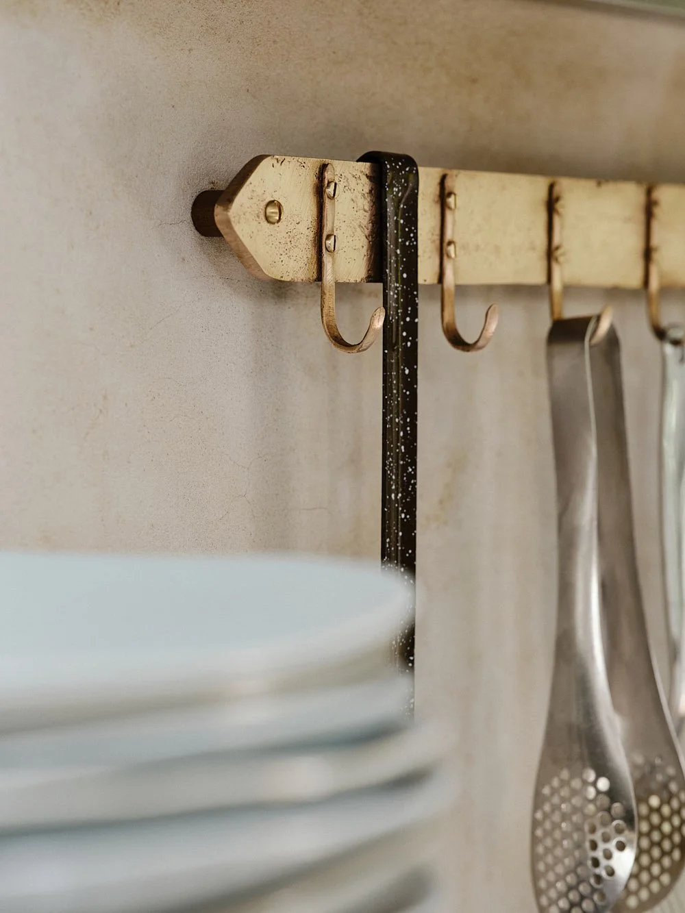 Close-up of the rack’s end showing a pasta spoon hanging from one of the sand-cast bronze hooks.