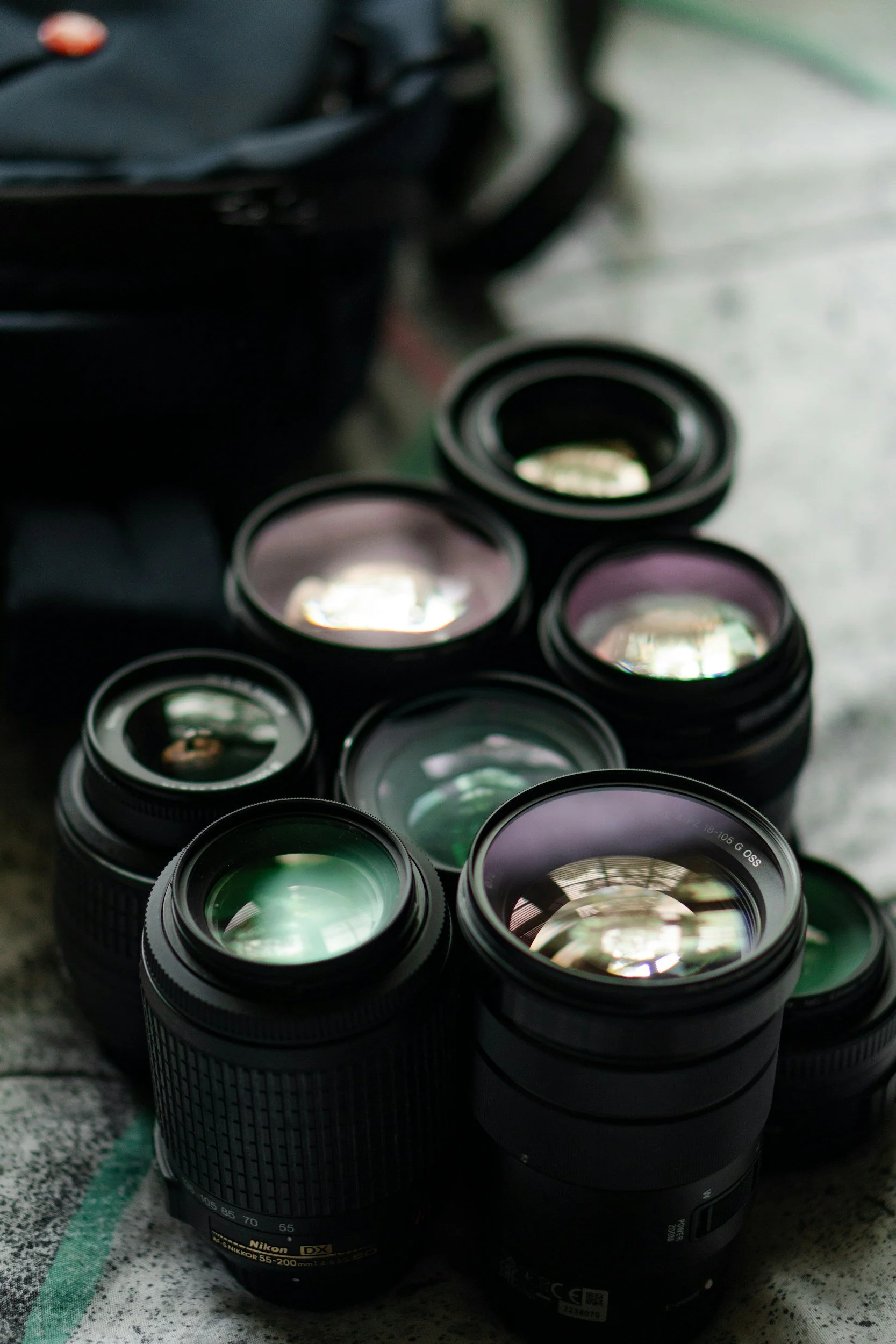 Camera lenses stacked on a cloth surface with a blurred black bag in the background.
