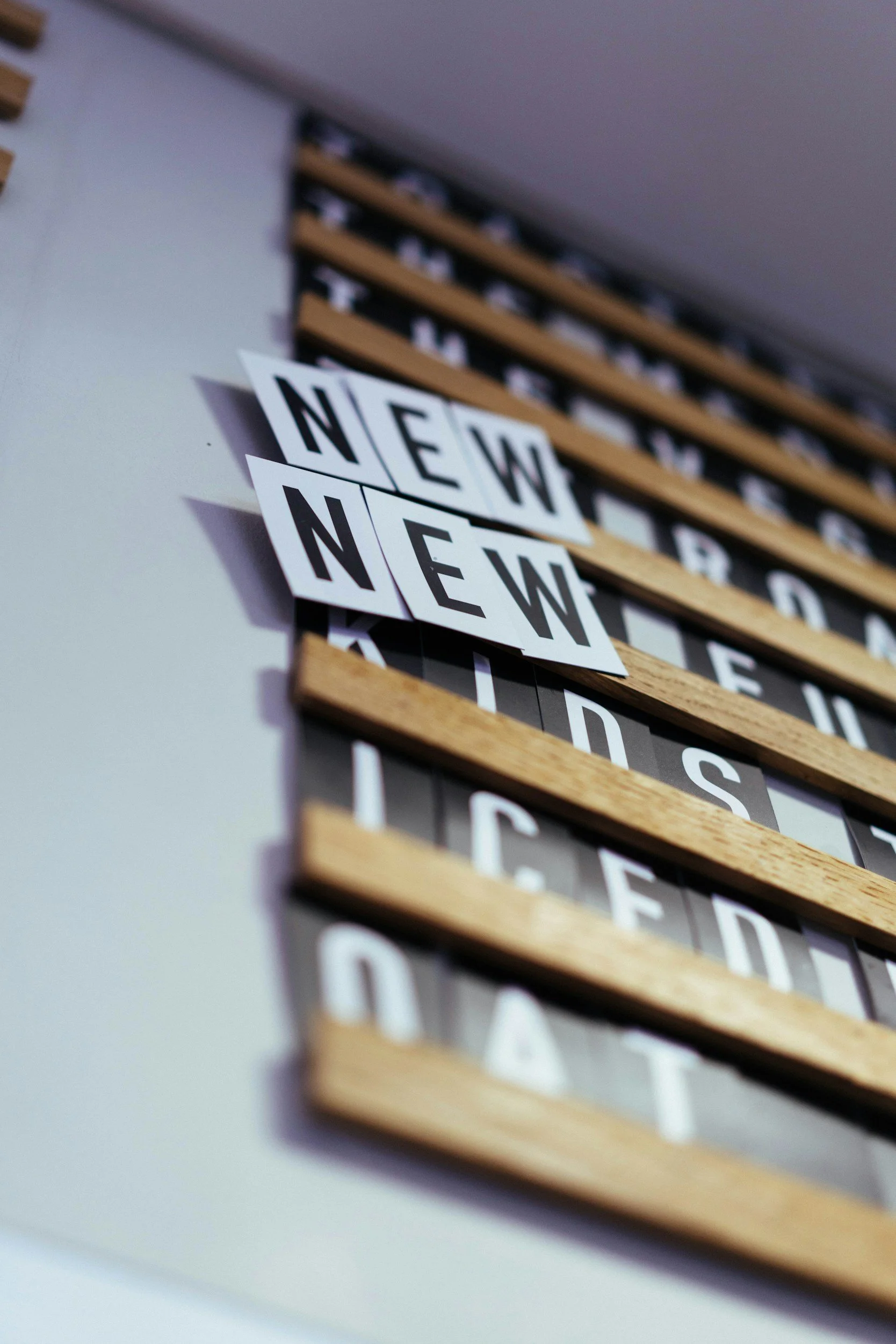 Close-up of a wall-mounted letterboard displaying the word "NEW" in black letters on white background cards.