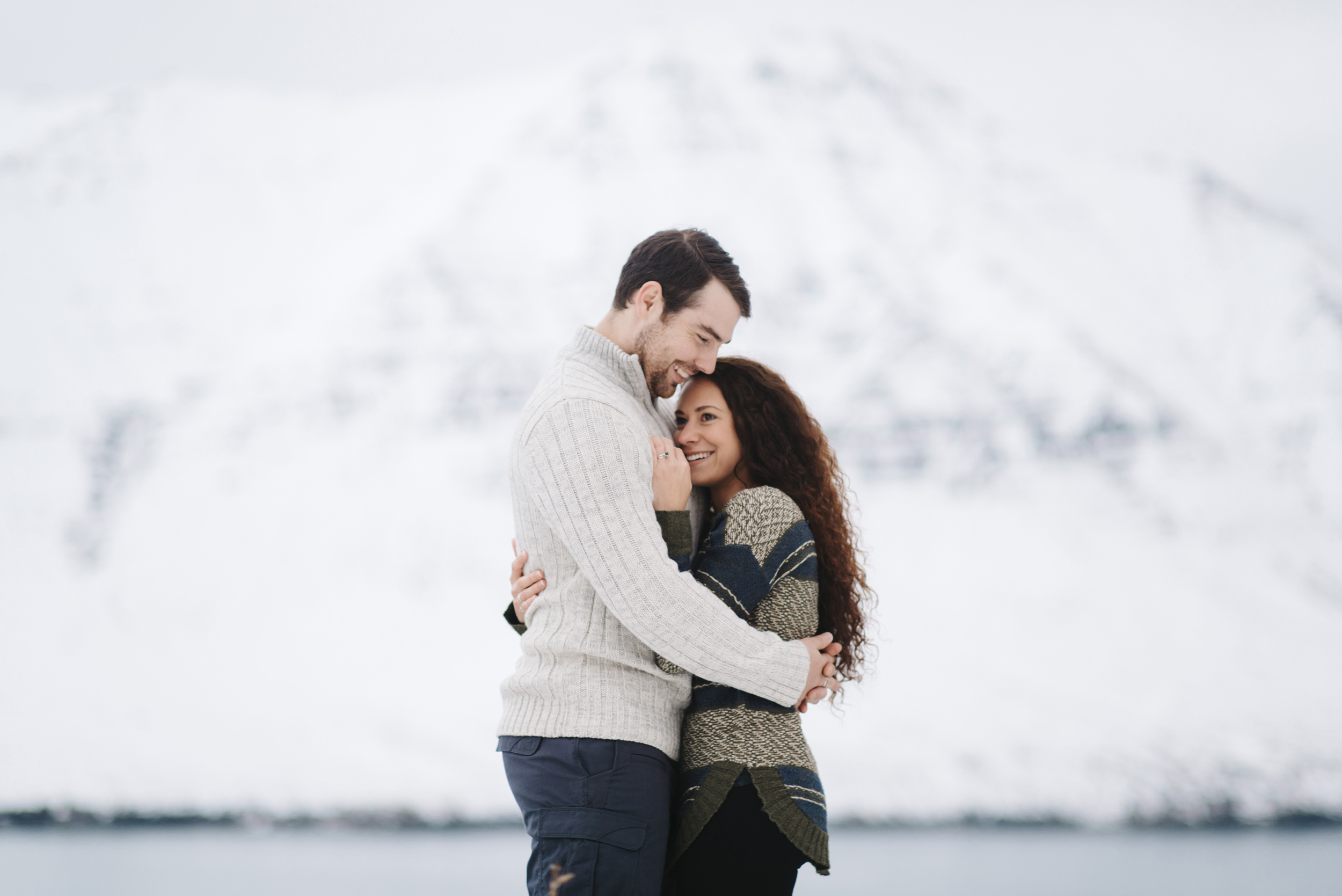 Couple in love cuddle in front of ice covered mountain Fjords during honeymoon photography by Iceland Elopement Photographer Colby and Jess colbyandjess.com