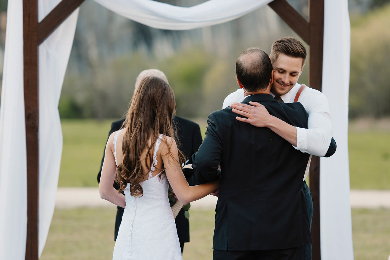 The father of the bride hugs the groom as he gives away his daughter during a Buffalo River Wedding with Arkansas Adventure Destination Elopement Photographers Colby and Jess