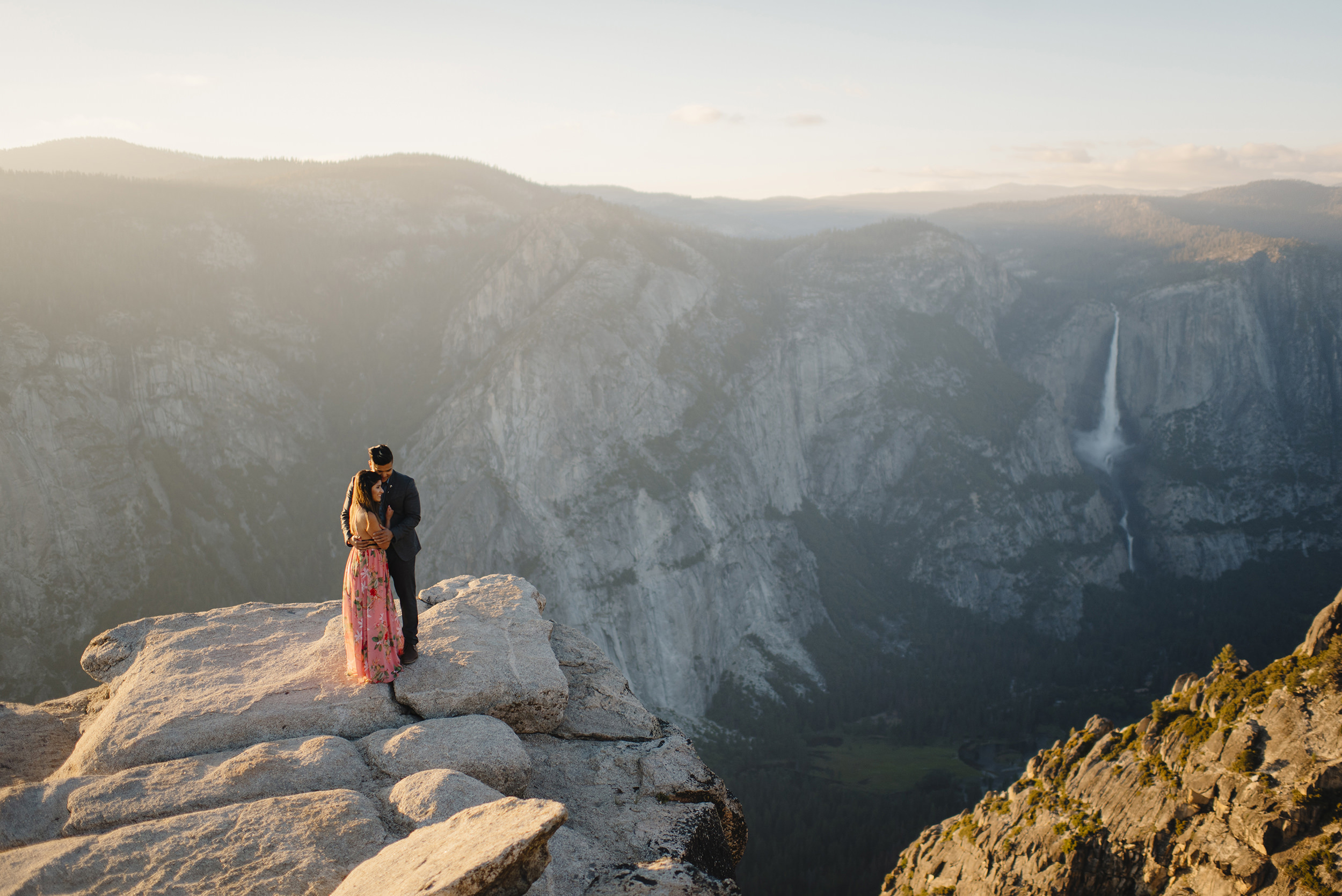 Adventurous couple snuggle on edge of Taft Point overlooking Yosemite Falls during engagement photography by Yosemite Wedding Photographers Colby and Jess colbyandjess.com