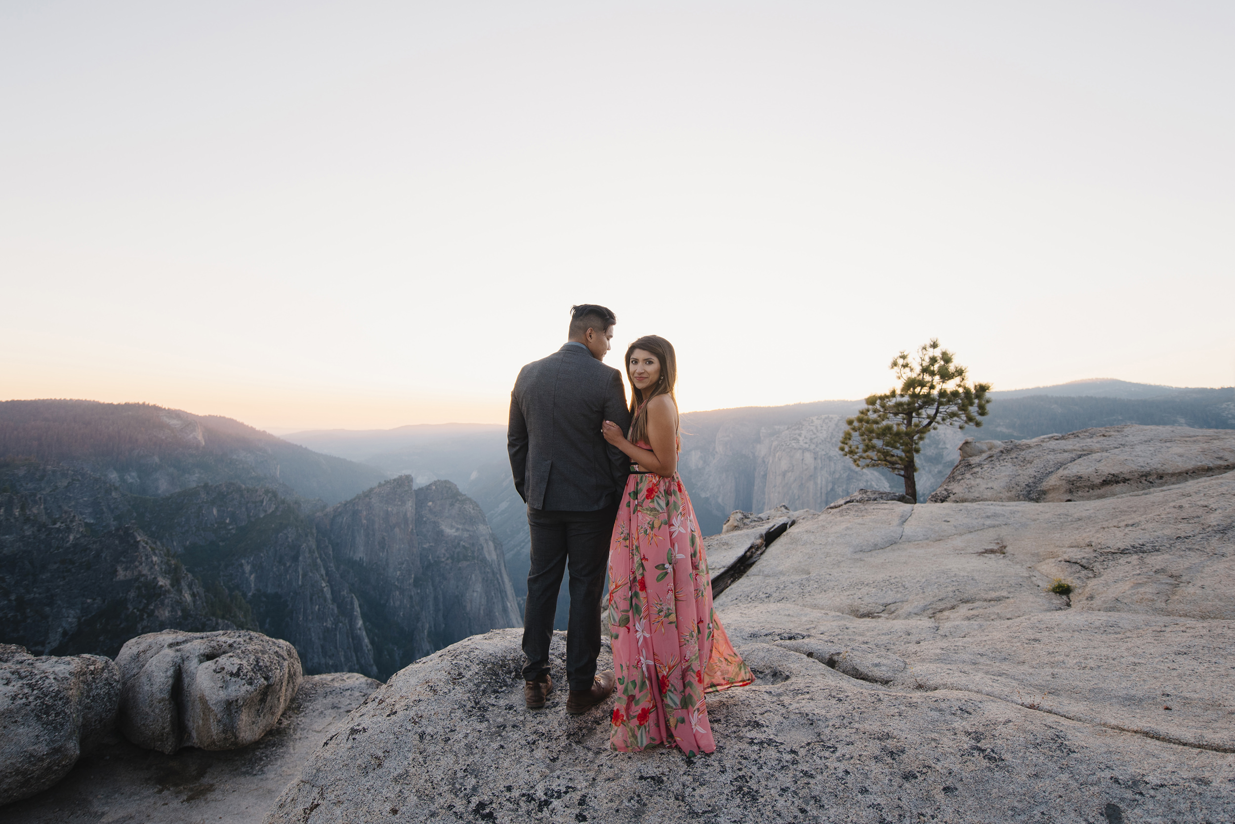 She glances back over her shoulder as they watch the sunset from Taft Point during engagement photography by Yosemite Wedding Photographers Colby and Jess colbyandjess.com