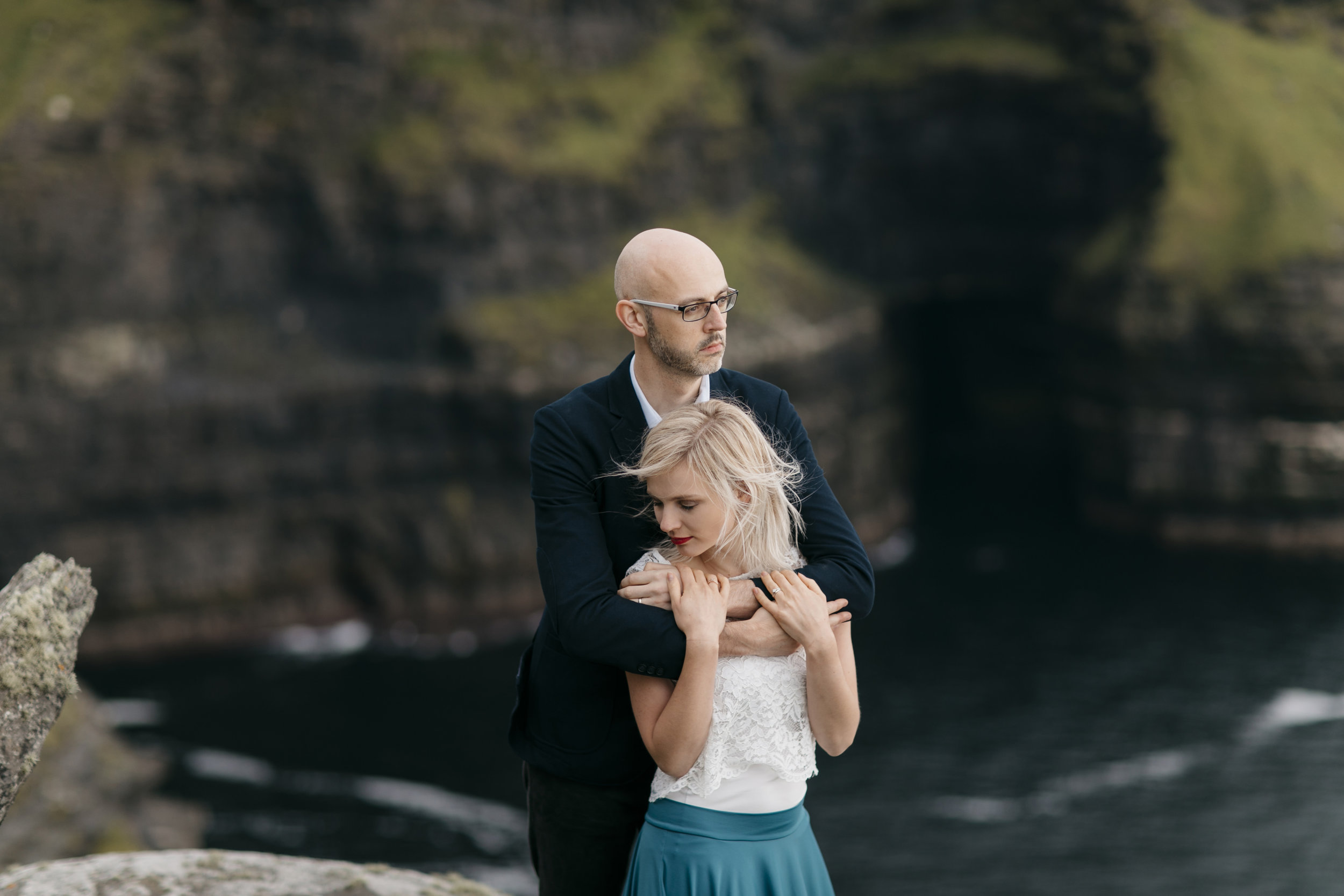 engaged couple snuggles on the edge of cliffs of moher during photography session by adventure elopement photographer Colby and Jess