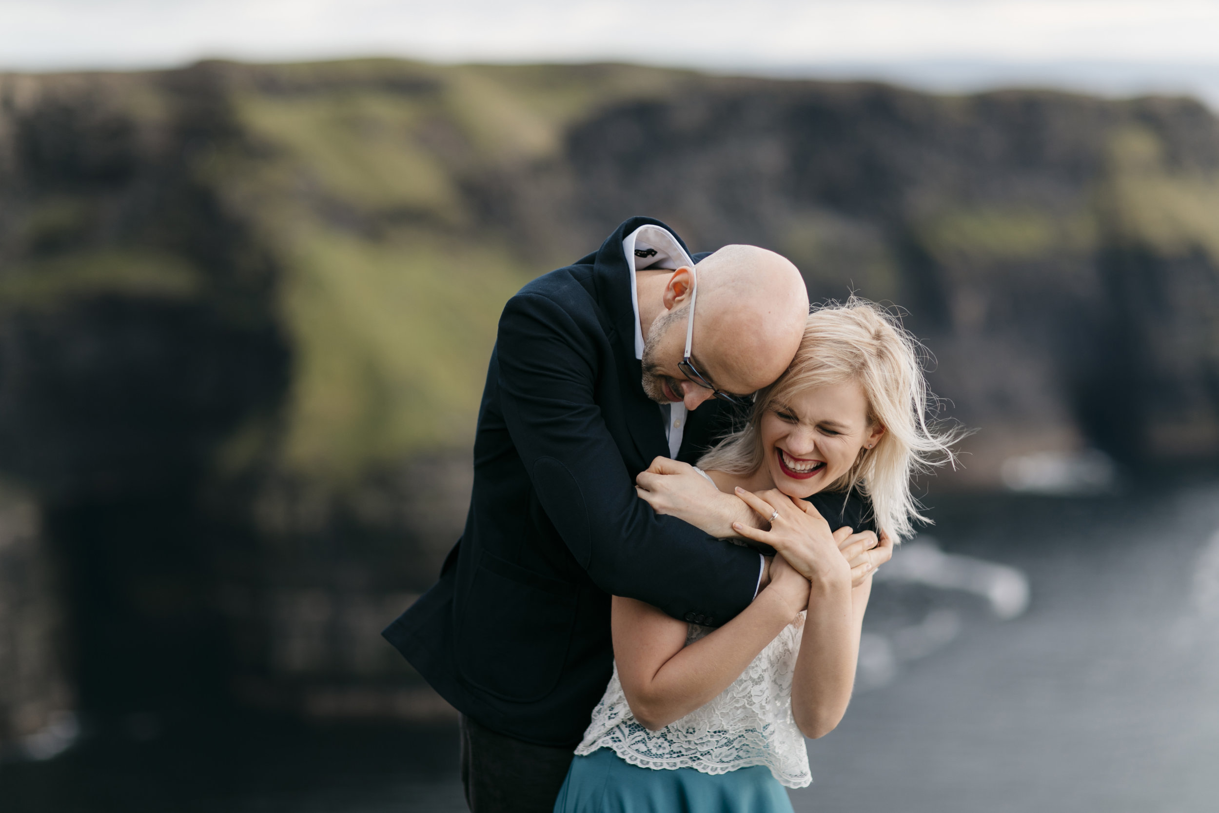 Man and woman laugh together during adventure photography session by cliffs of moher elopement photographer Colby and Jess