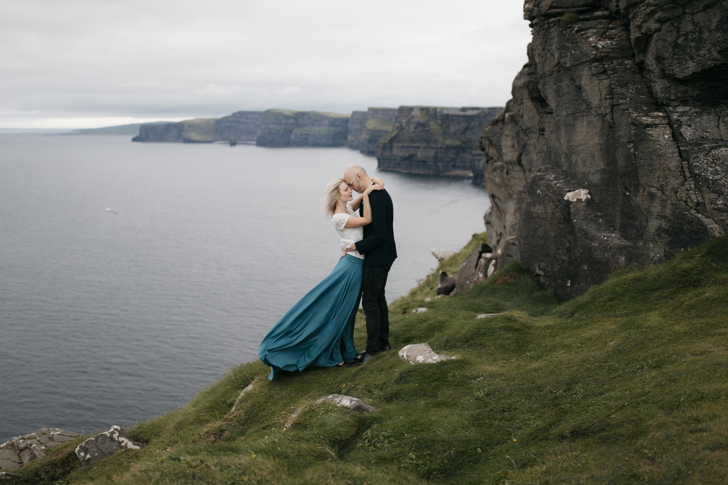 A beautiful couple clings to each other on the Cliffs of Moher during adventure photography session by Ireland Elopement photographers Colby and Jess