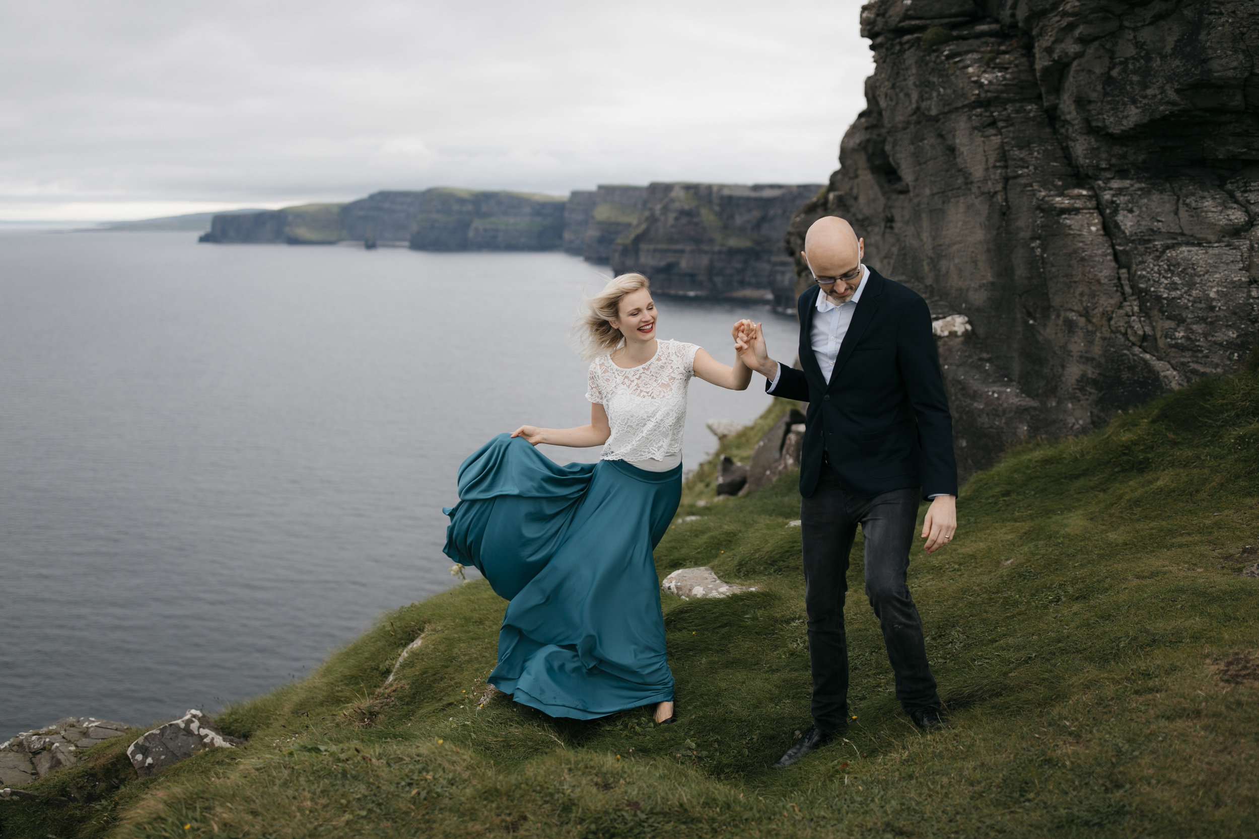 A man leads his wife along Cliffs of Moher during anniversary photography session by adventure wedding photographer colby and jess 