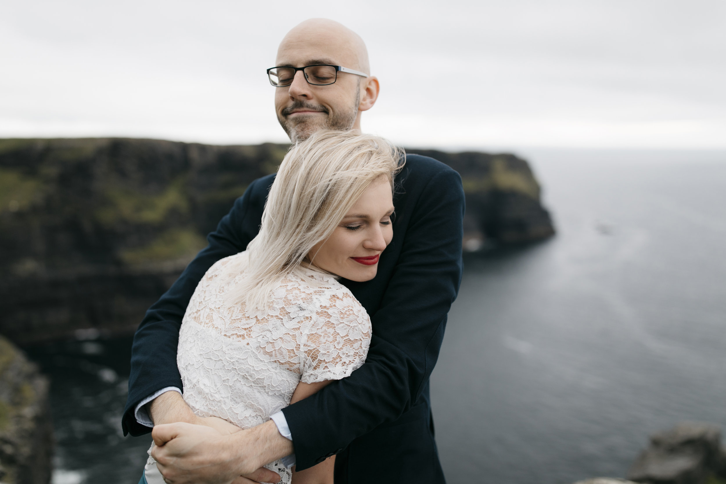 An adventurous couple hold each other tight at the Cliffs of Moher during anniversary adventure session by Ireland Elopement Photographers Colby and Jess