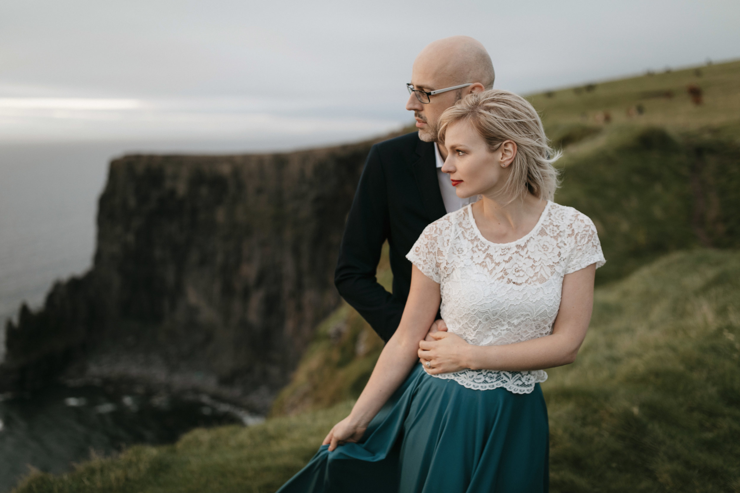 Looking out to the sea, an adventurous couple stand at the Cliffs of Moher while being photographed by Ireland Elopement Photographers Colby and Jess