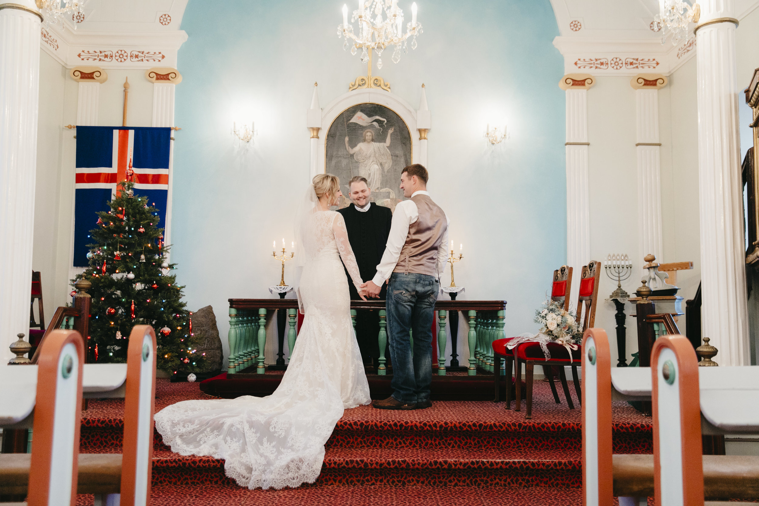 A couple stands in the front of the Hvalsneskirkja Church in Iceland during their Iceland Elopement Wedding by photographers Colby and Jess.