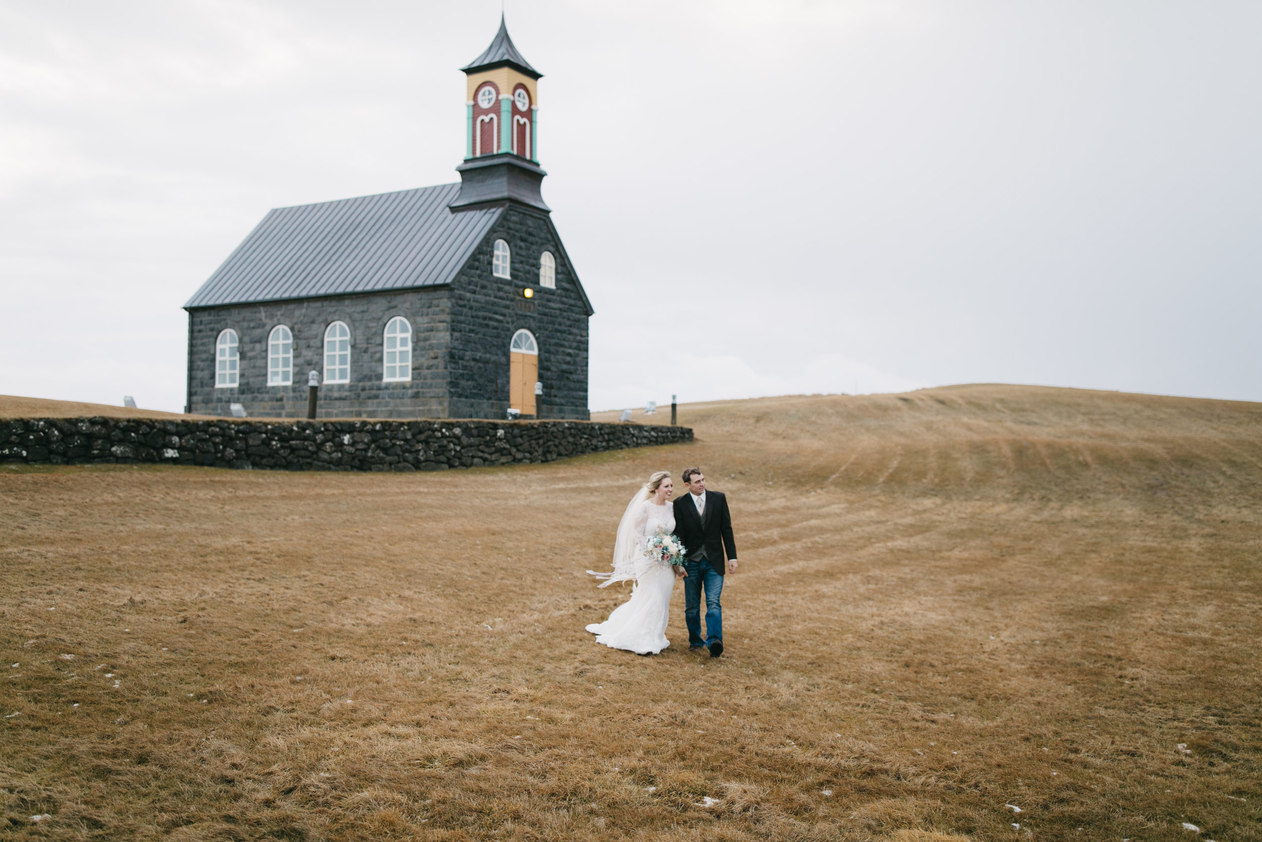 A couple who just eloped in Iceland stand in front of Hvalsneskirkja Church with their Iceland Elopement photographers Colby and Jess, colbyandjess.com