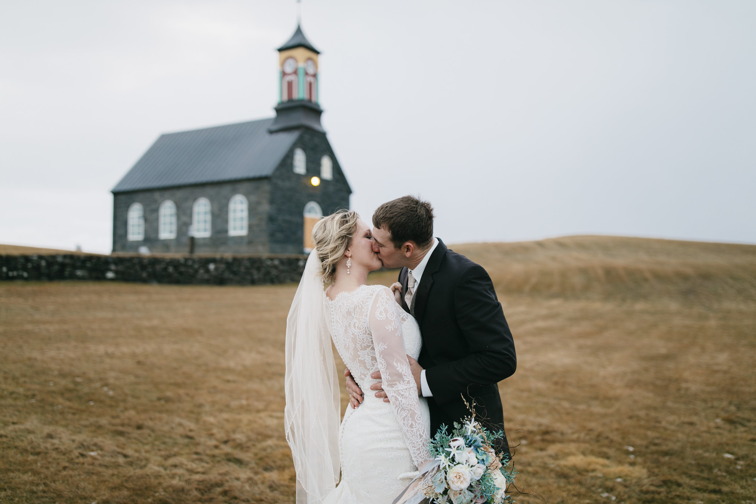 After their wedding in Hvalsneskirkja Church this couple kiss to celebrate with their Iceland Elopement photographers Colby and Jess, colbyandjess.com