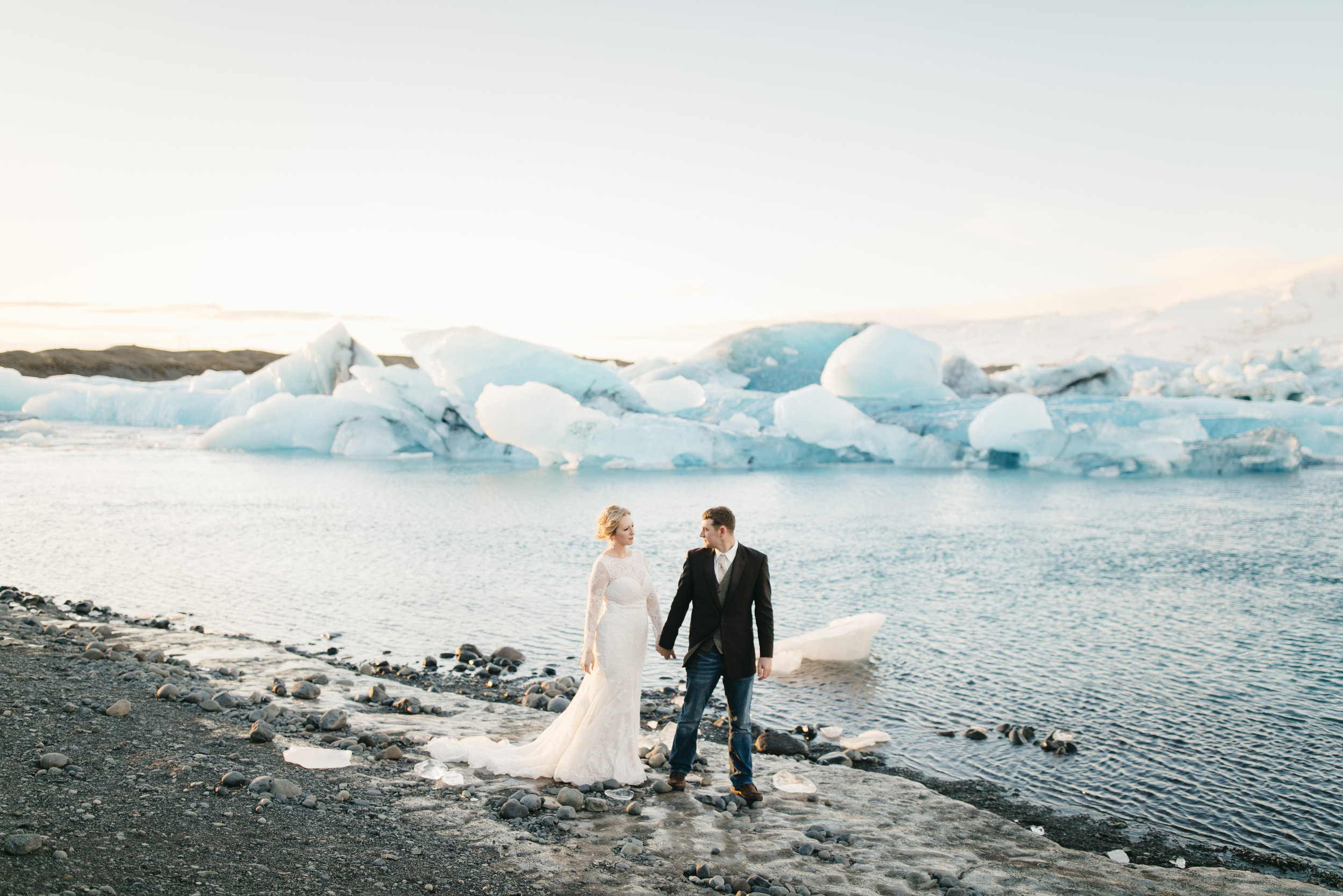 A happy couple walks along beach beside glaciers during Iceland Elopement Photography session by Colby and Jess.