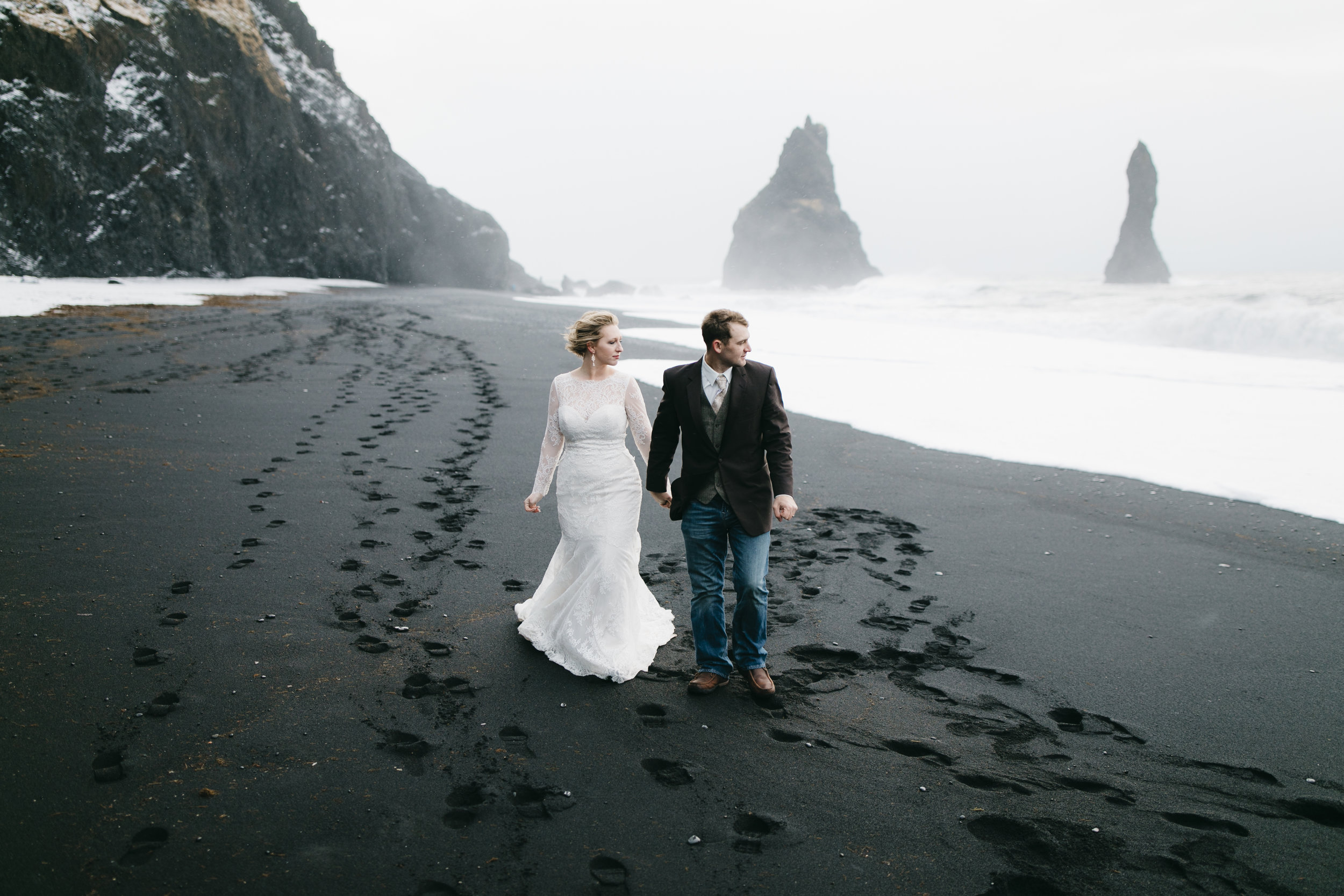 A man and his wife walk along the black sand beaches in Vik after their adventure elopement with Iceland wedding photographers Colby and Jess, colbyandjess.com