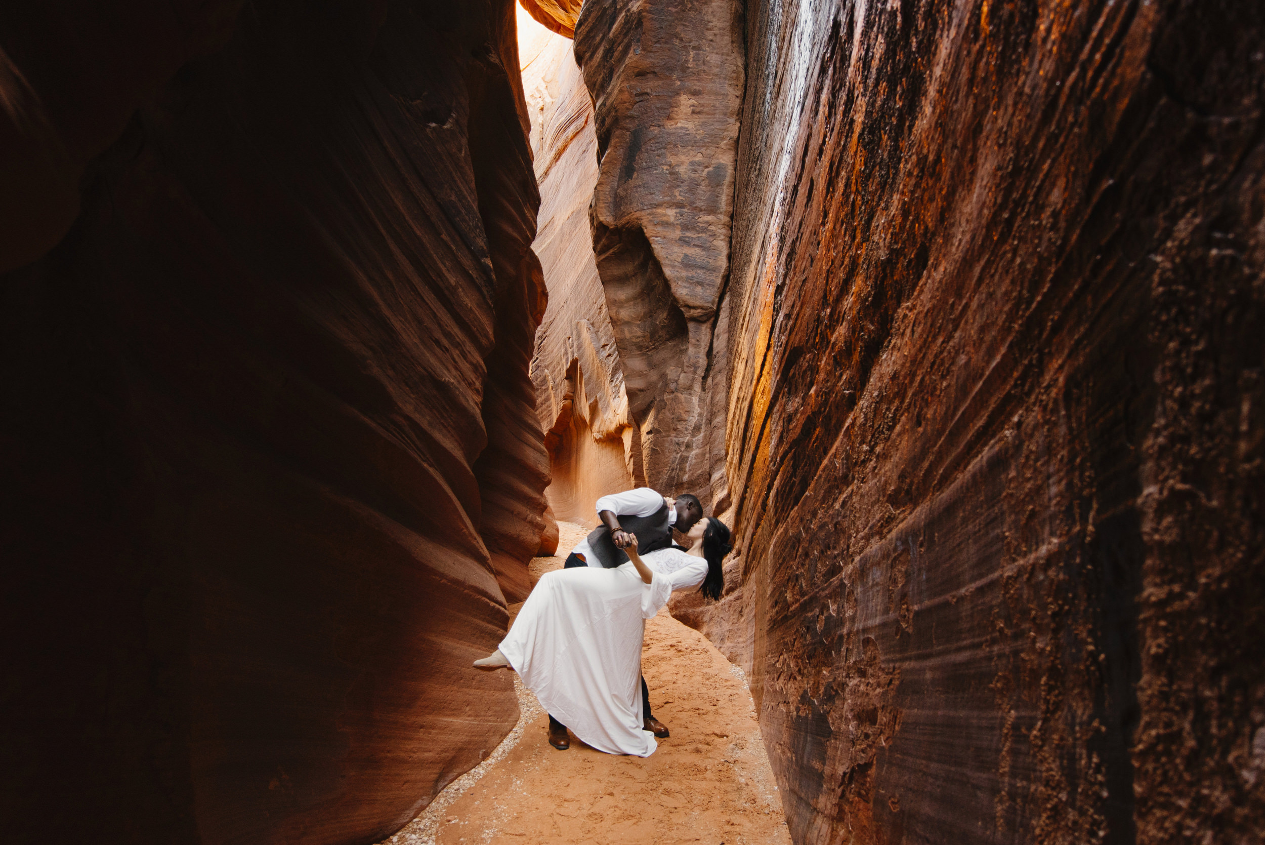 A man dips his wife and kisses her while dancing in a slot canyon during their Antelope Canyon couples adventure photography session with Utah Destination Elopement Photographer Colby and Jess