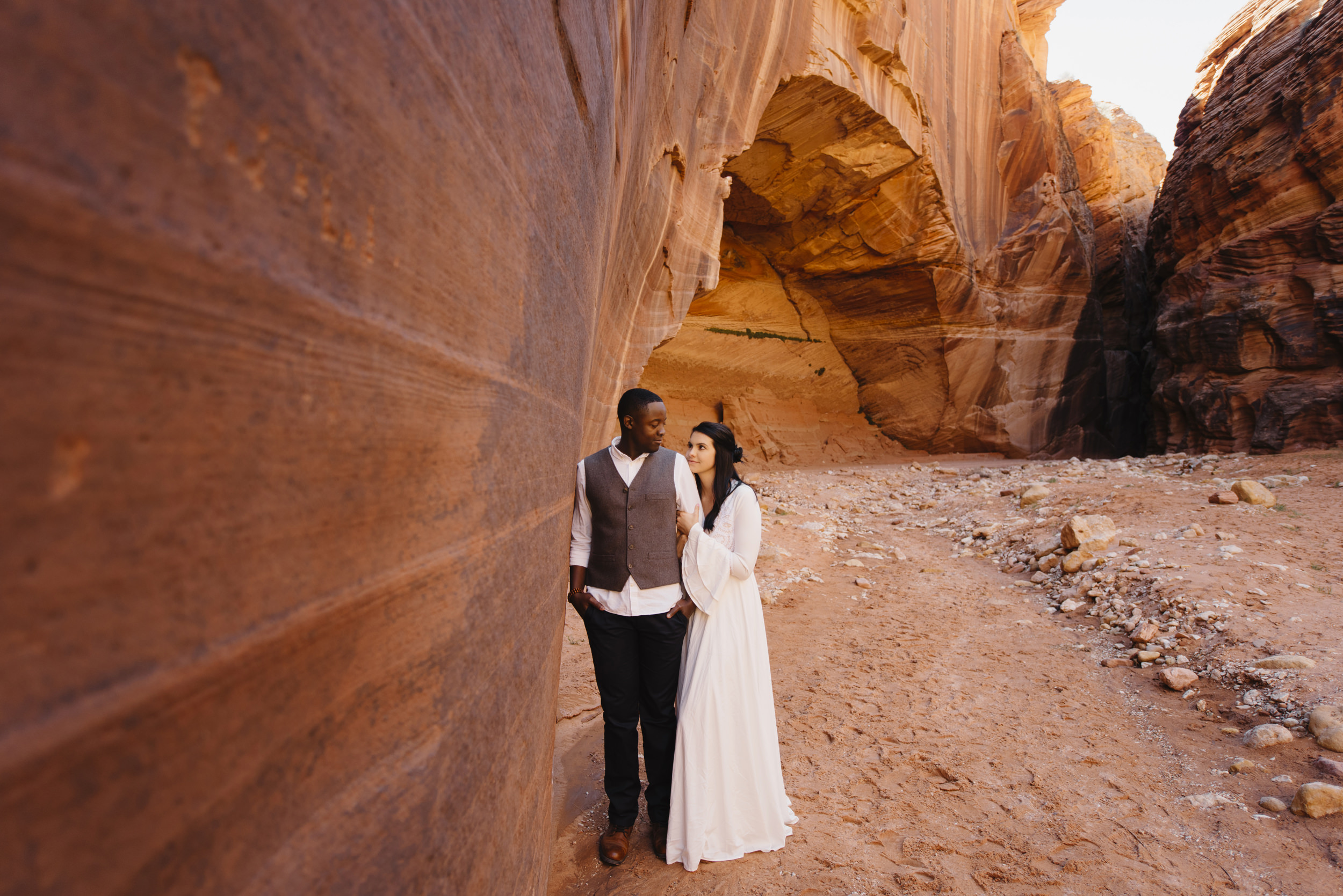 A couple embraces beside the red rock of Antelope Canyon during their Adventure couples photography session by Utah Destination Elopement Photographers Colby and Jess