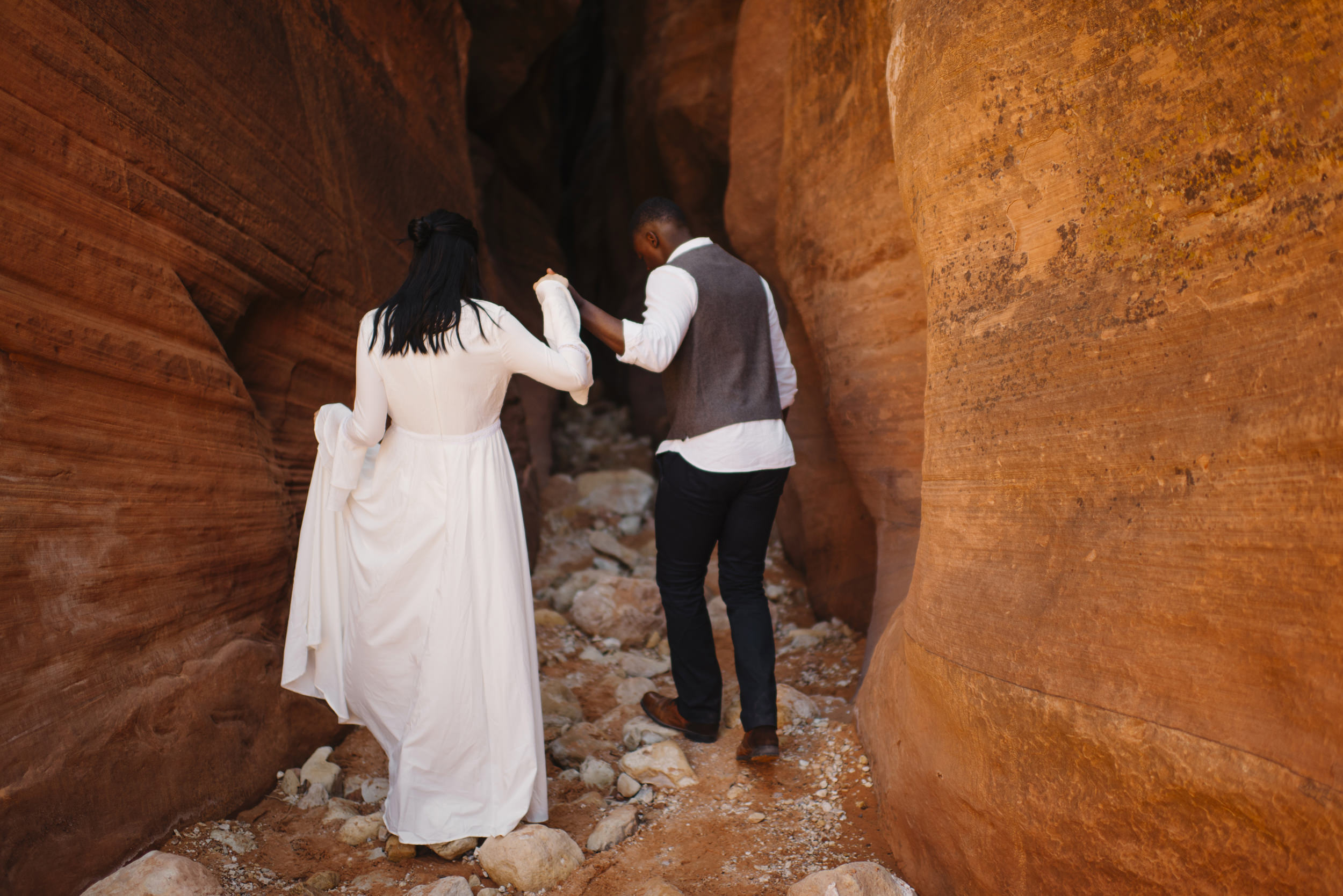 A man holds his wife's hand leading her into a slot canyon during their Antelope Canyon Couple's Adventure Photography Session with Utah Destination Elopement Photographer Colby and Jess