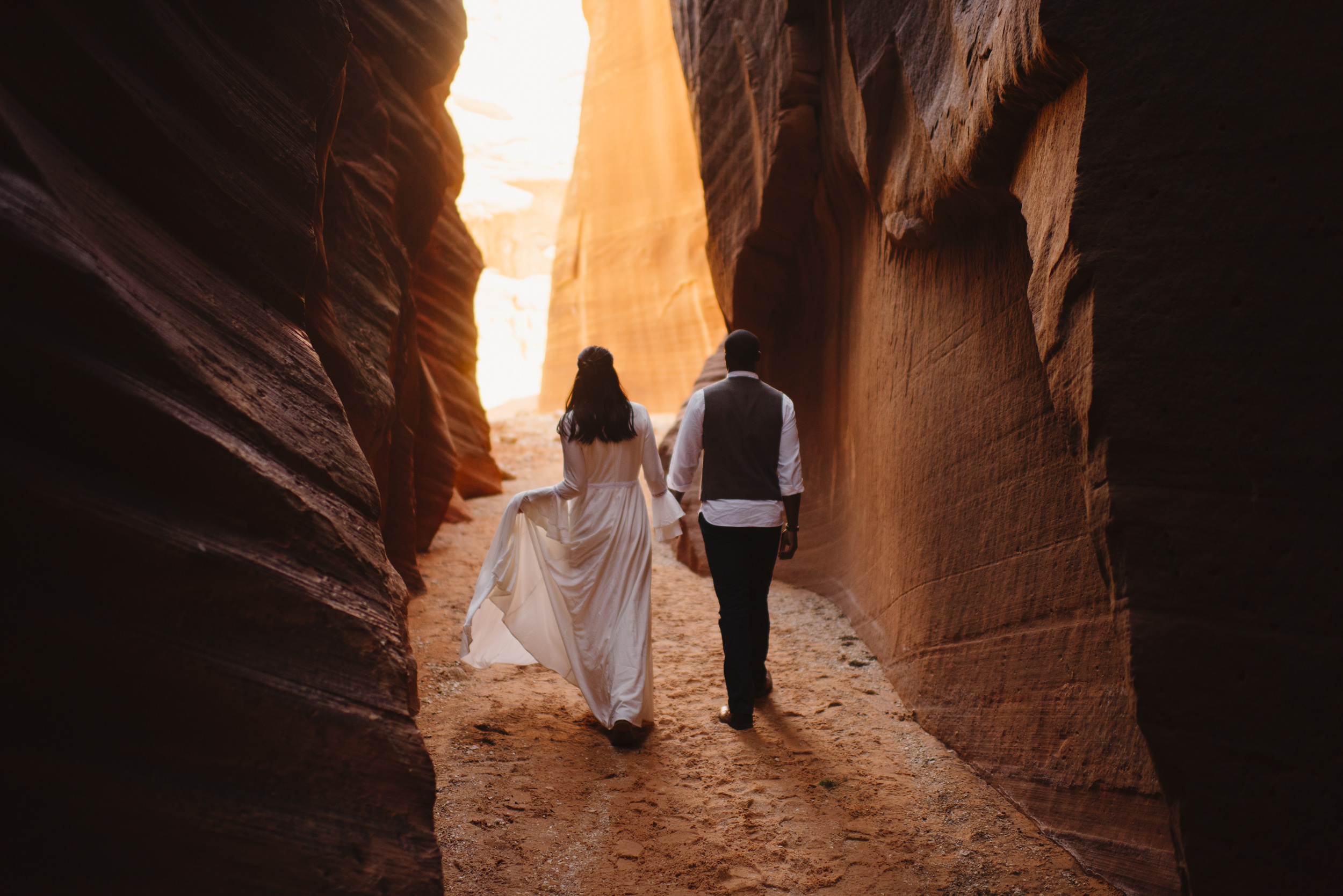 A couple is holding hands while exploring a slot canyon during their adventure engagement photography session with Utah Destination Elopement Photographer Colby and Jess