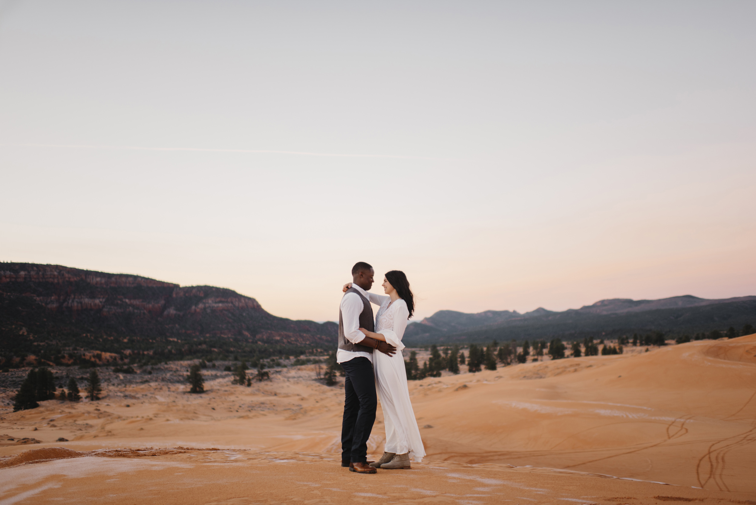 A couple shares a dance at pink coral sand dunes during their adventure couples photography session by Utah Destination Elopement Photographer Colby and Jess