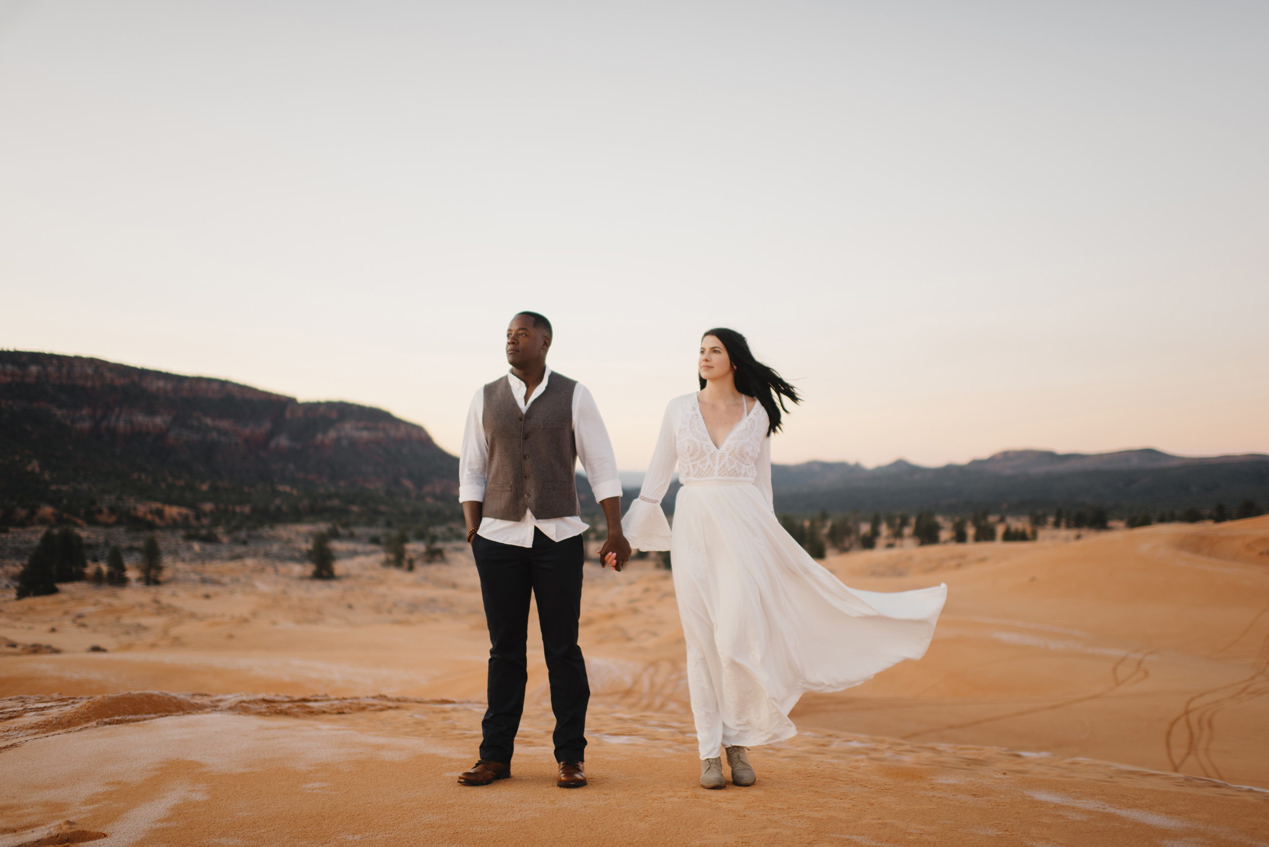 A couple holds hands while exploring coral pink sand dunes with Utah Destination Elopement Photographer Colby and Jess