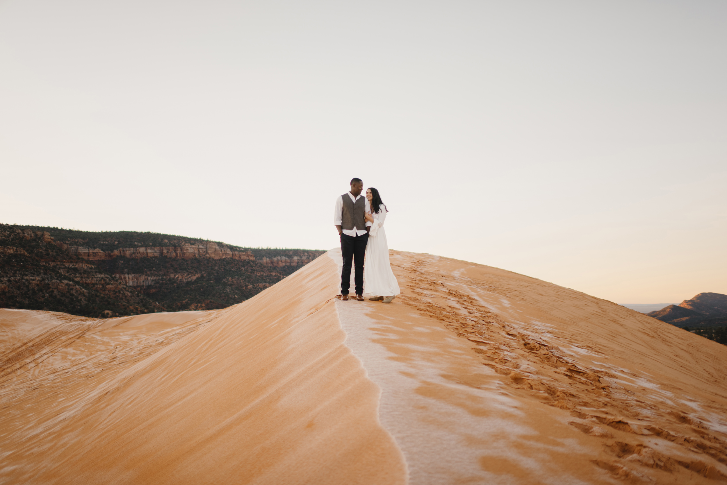 A couple stands side by side during their Coral Pink Sand Dunes adventure engagement photography session by Utah Destination Elopement Photographer Colby and Jess