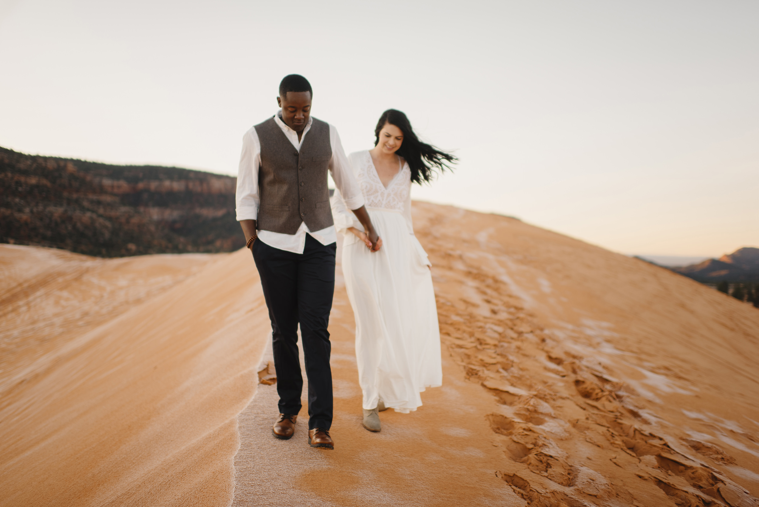 Holding hands a couple smiles during their Coral Pink Sand Dunes Engagement Photography Session by Utah Destination Elopement Photographer Colby and Jess