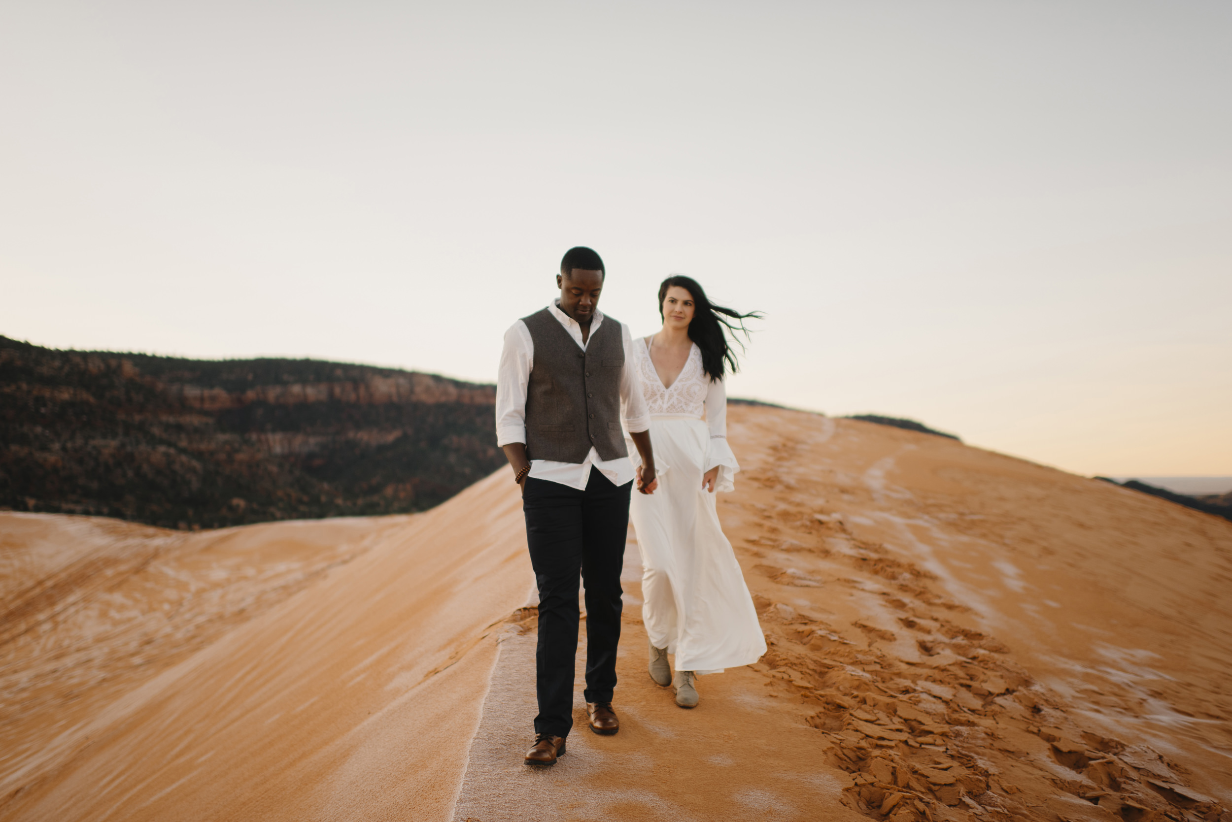 A man and woman hold hands exploring during their Coral Pink Sand Dunes Engagement Photography Session with Utah Destination Elopement Photographer Colby and Jess
