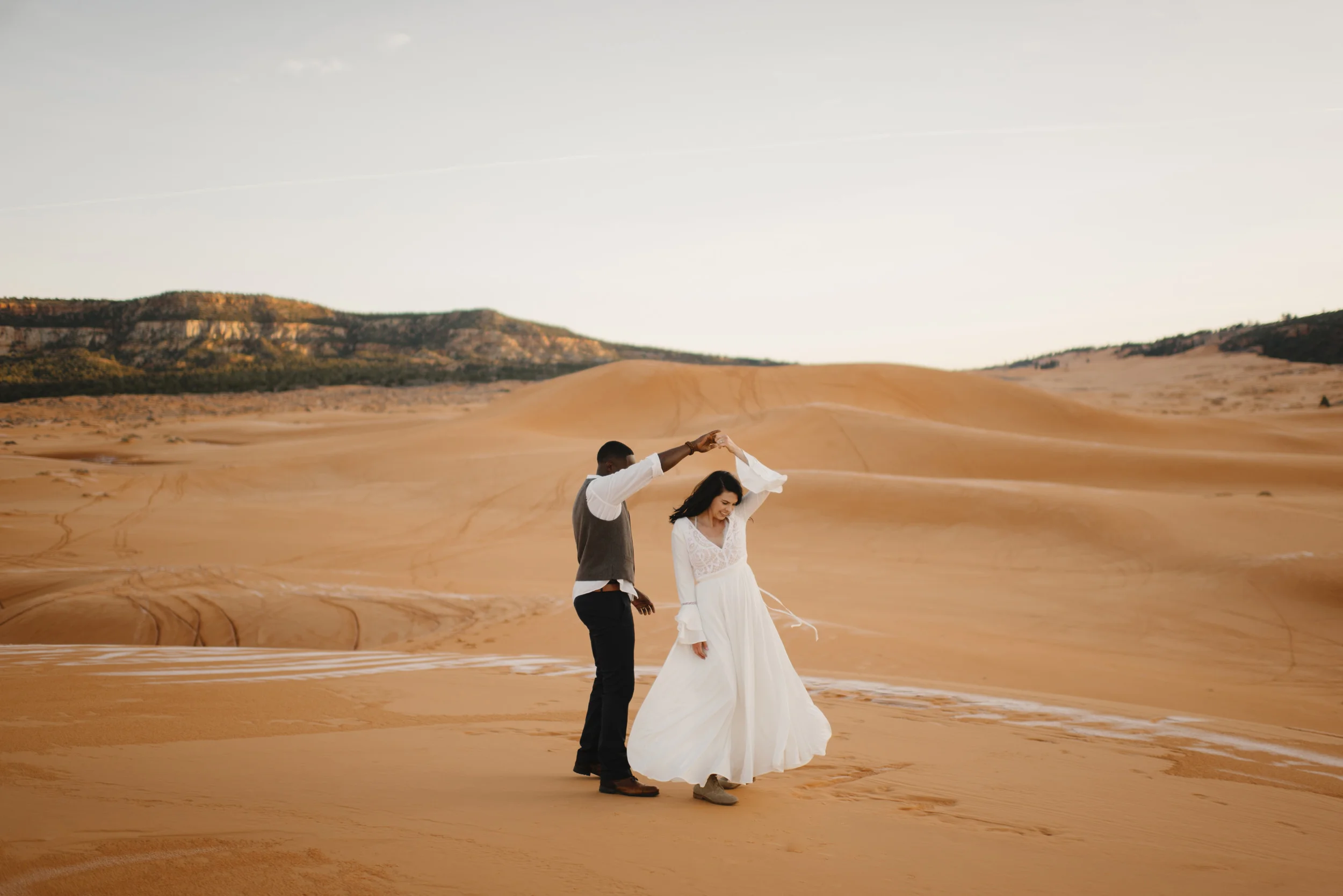 A couple dances in Coral Pink Sand Dunes during their adventure engagement photography session by Utah Destination Elopement Photographer Colby and Jess