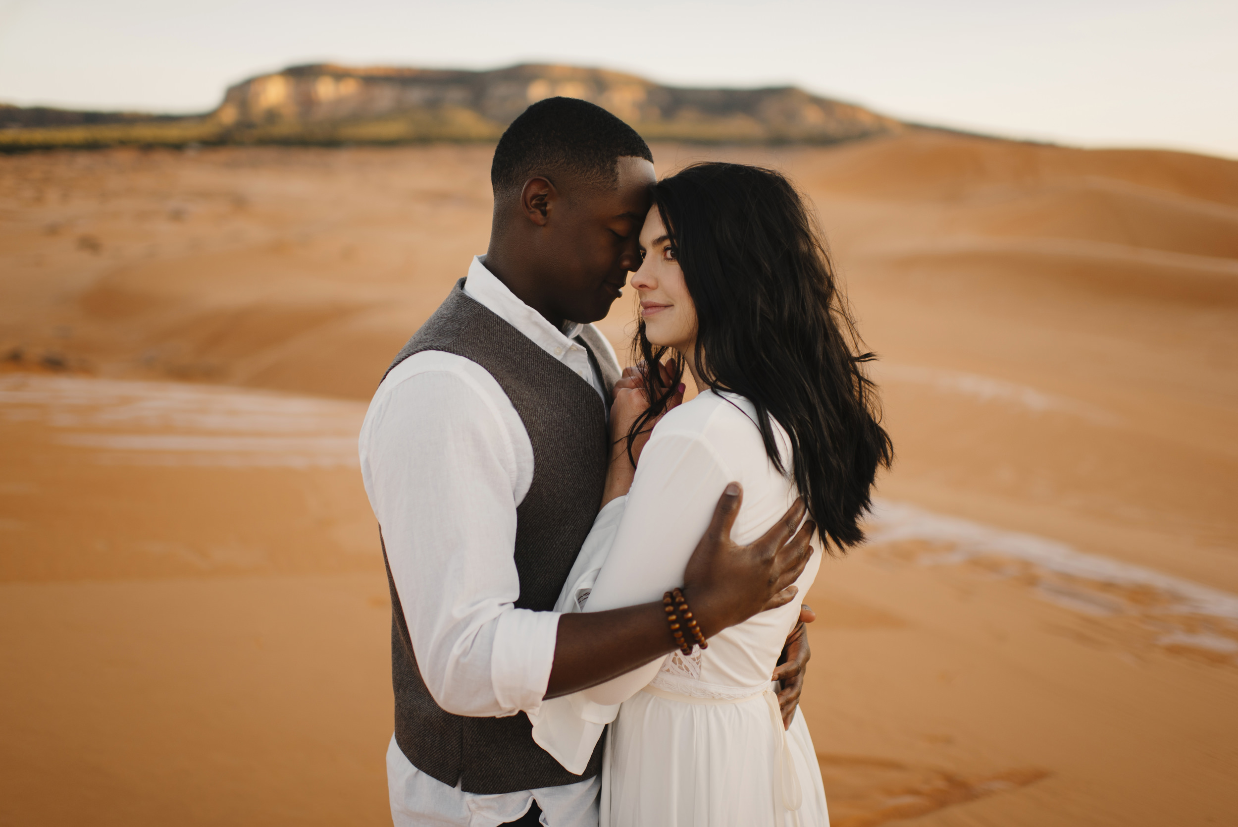 A man embraces his wife during their Anniversary Couples Adventure Photography Session with Utah Sand Dunes Destination Elopement Photographer Colby and Jess