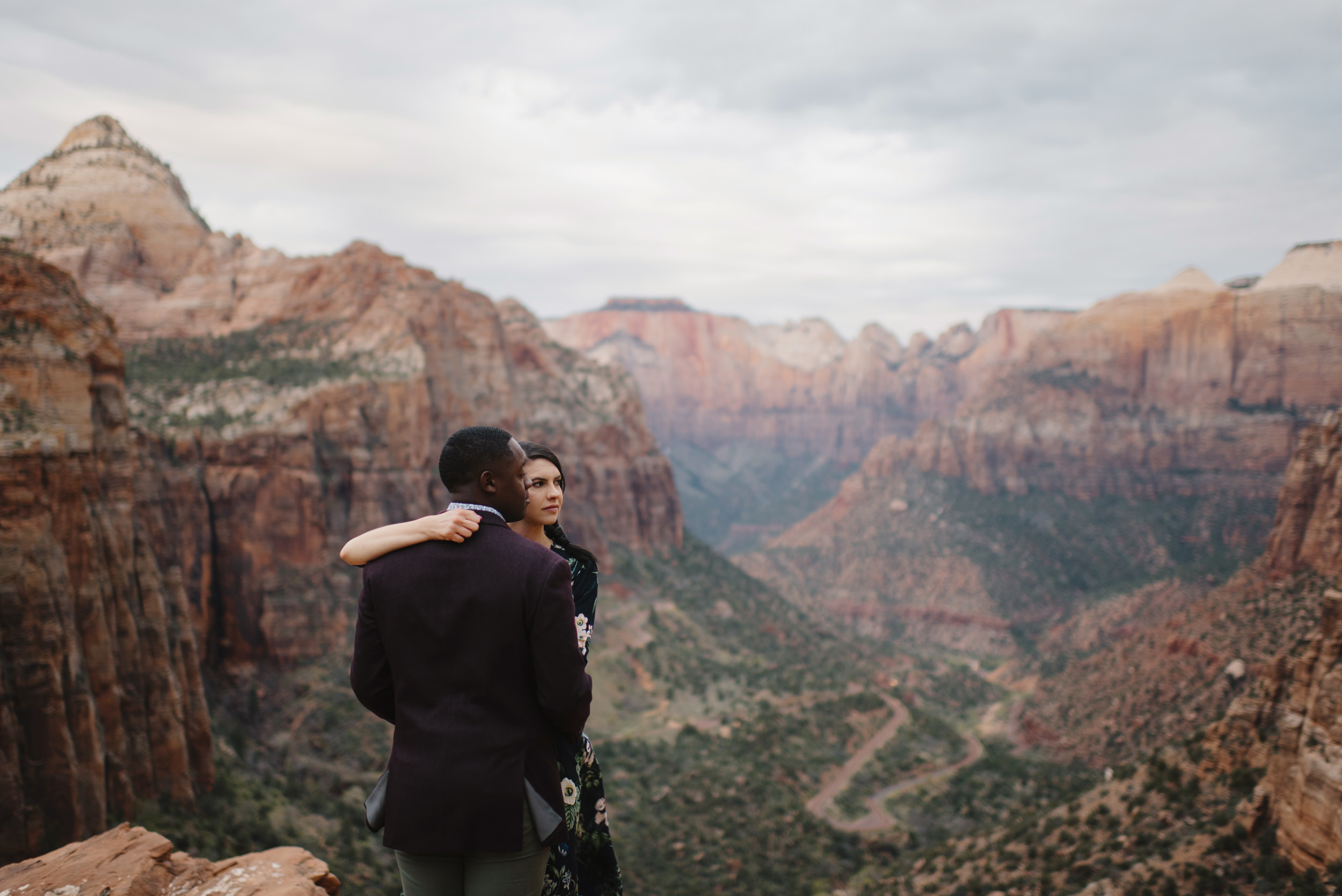 A man and woman look out from Angels Landing during their Zion Engagement Photography Session by Zion National Park Elopement Photographer Colby and Jess